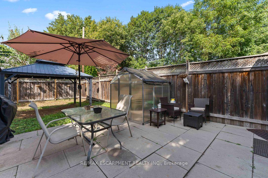 Backyard patio with umbrella-covered dining table, gazebo, greenhouse, and fenced seating area.