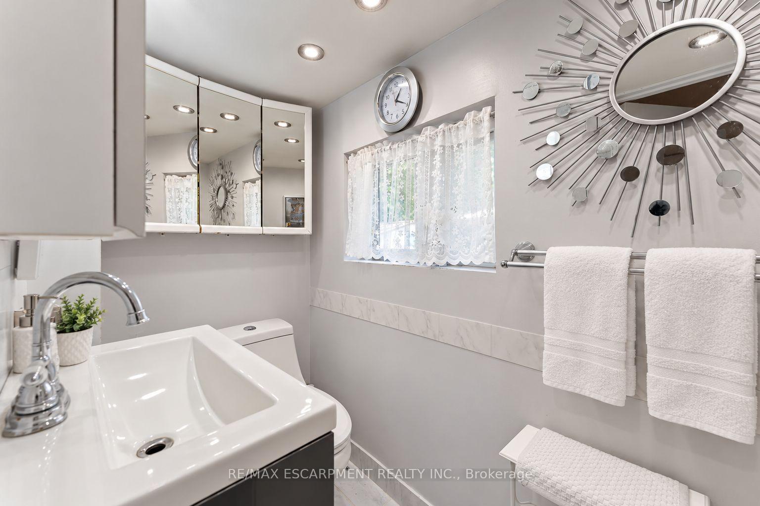 Bathroom with a white sink vanity, mirrored cabinet, and lace-curtained window.