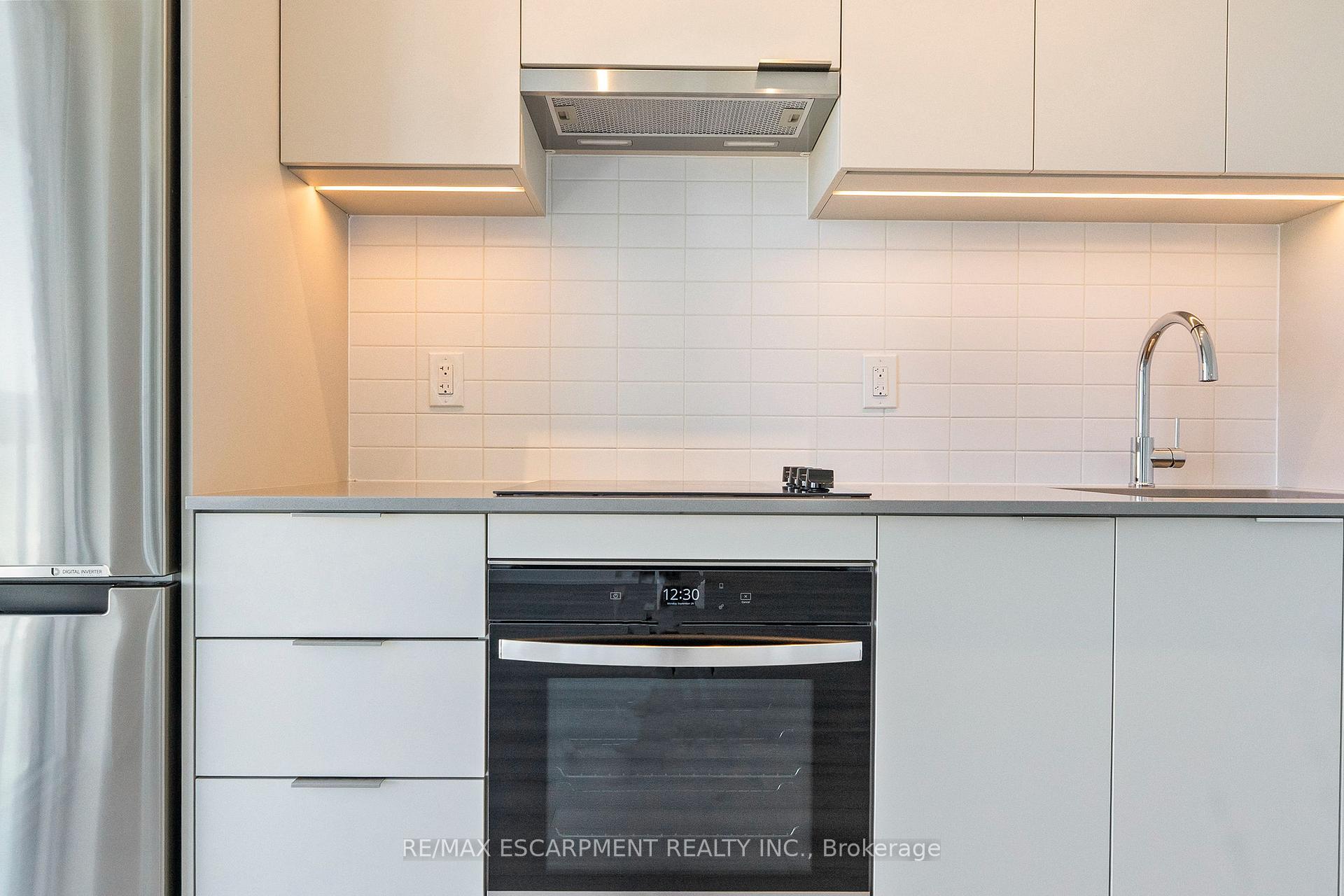 Modern kitchen with white cabinetry, tiled backsplash, stainless steel refrigerator, and black built-in oven.