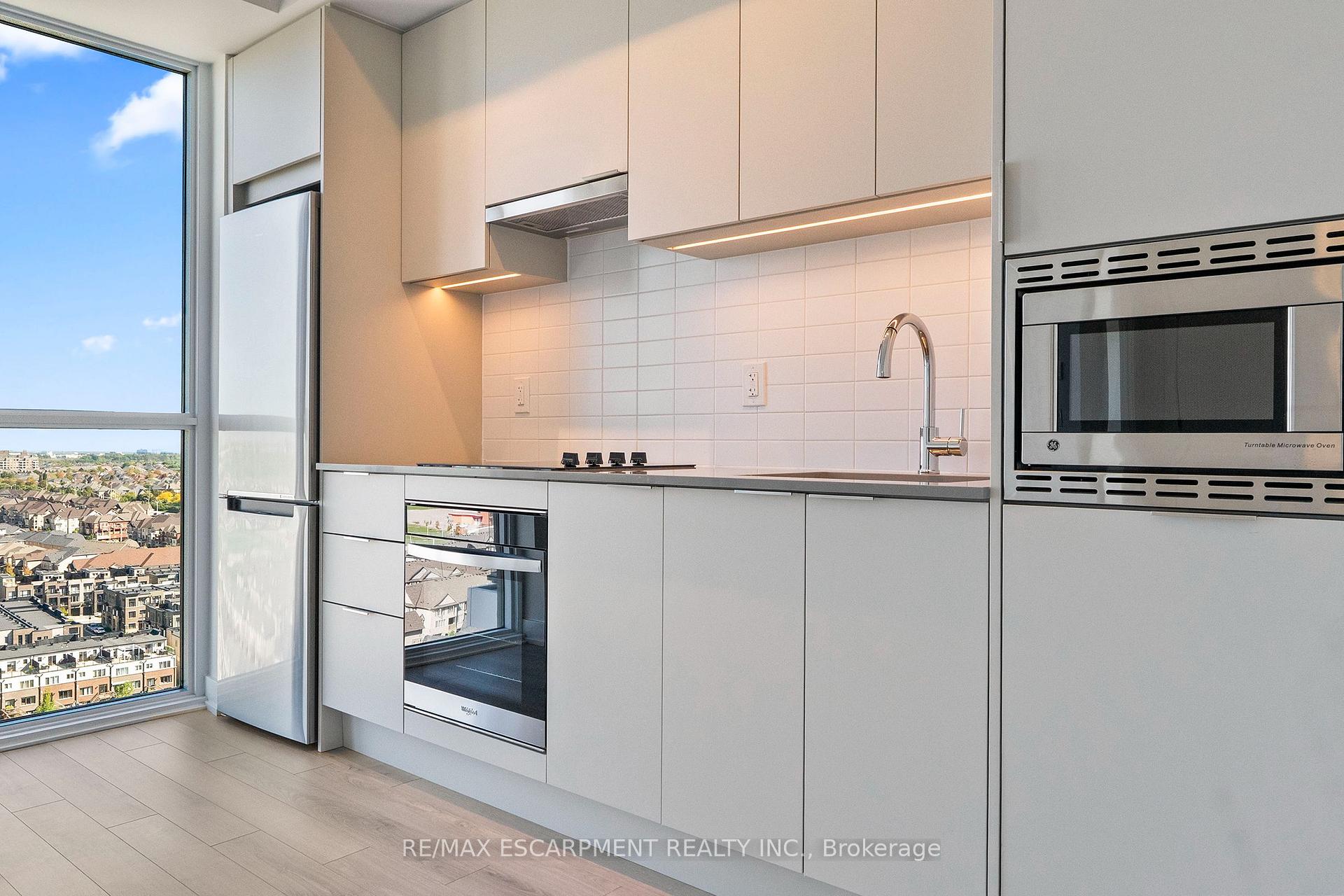 Modern condo kitchen with white cabinetry, stainless appliances, and a wide window overlooking the neighborhood.