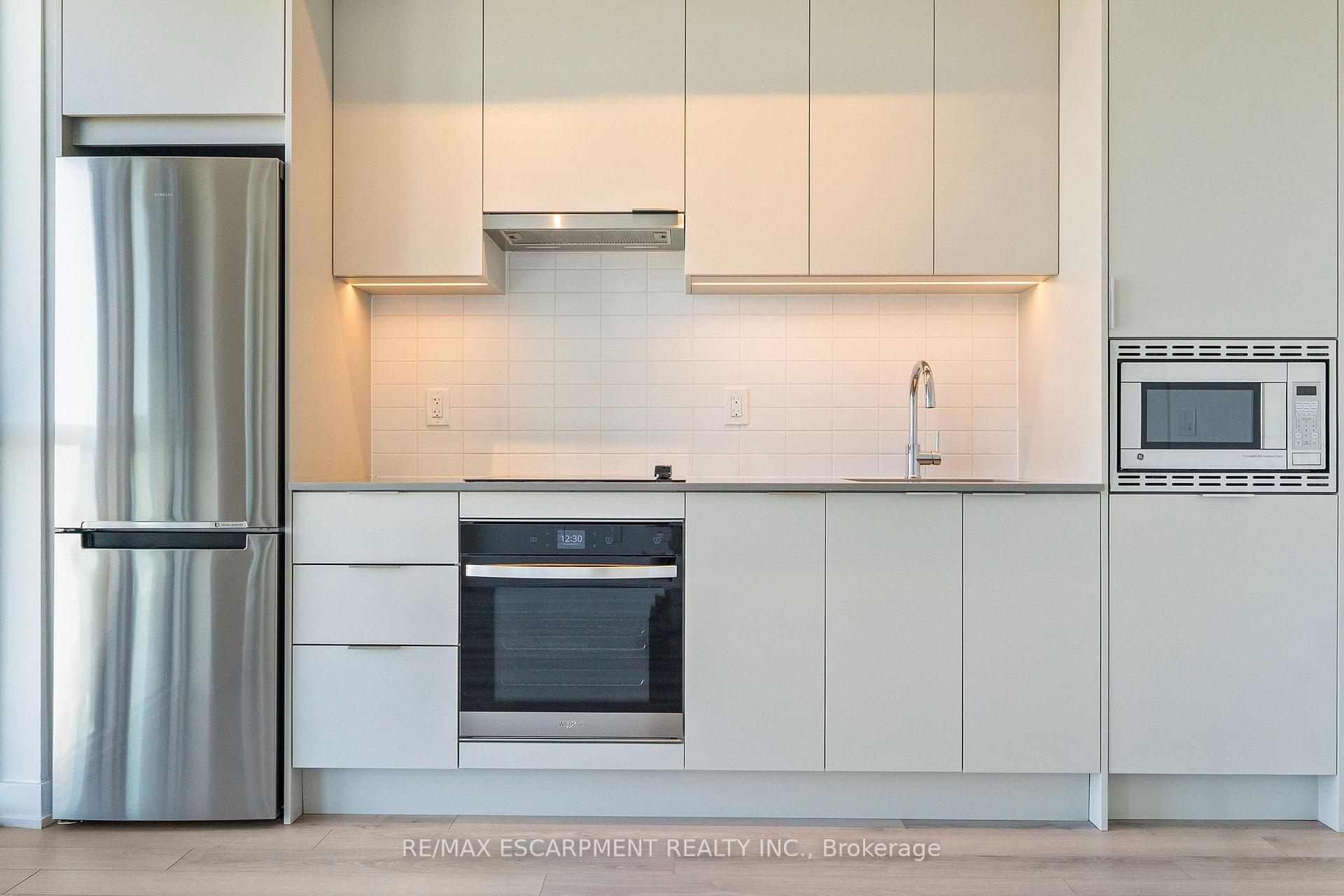 Modern condo kitchen with white cabinetry, stainless steel appliances, and a tiled backsplash.