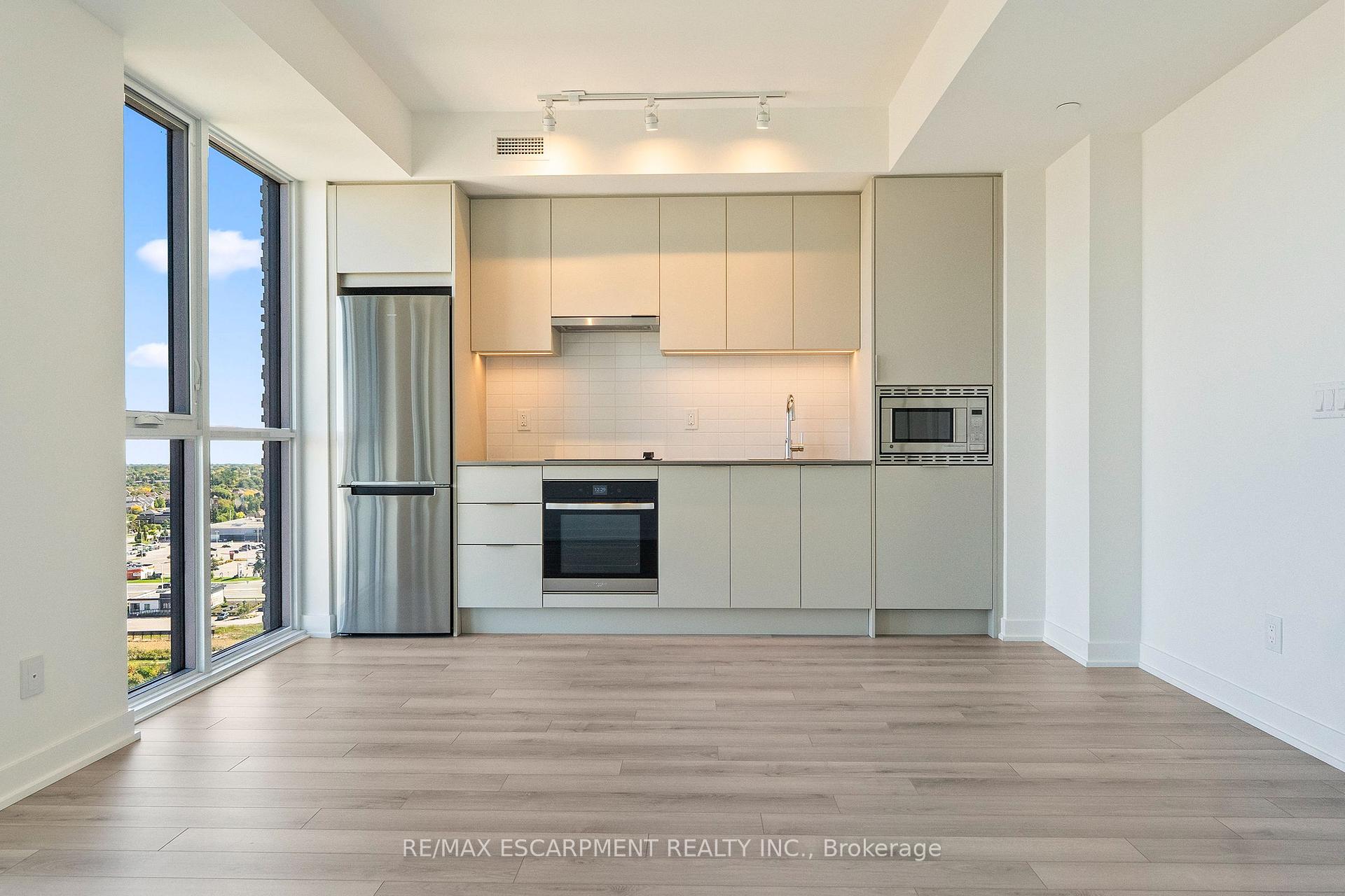 Modern condo kitchen with white cabinetry, stainless steel appliances, and tall windows overlooking the neighborhood.