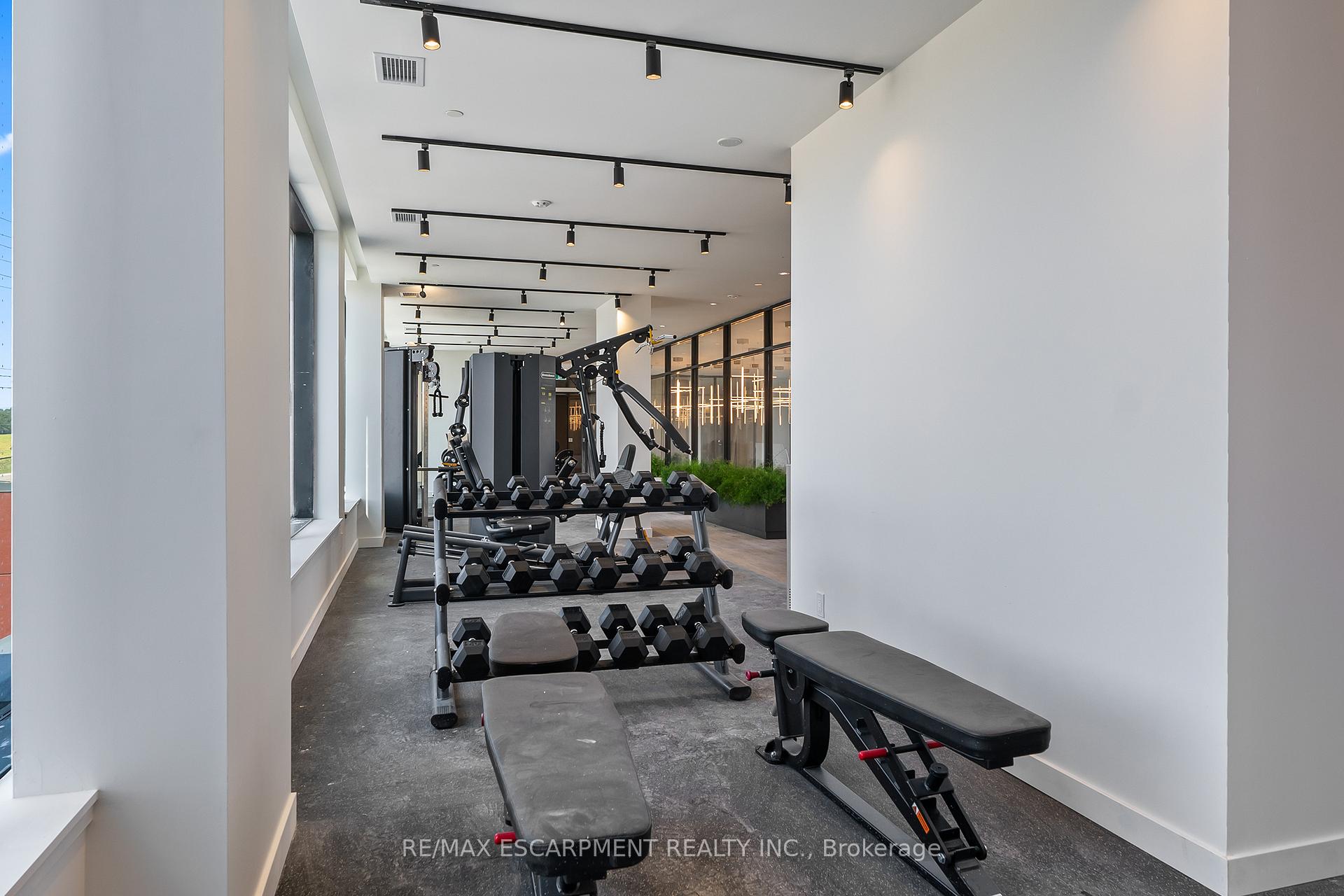 Fitness room with dumbbell racks, weight machines, and exercise benches beside large windows.