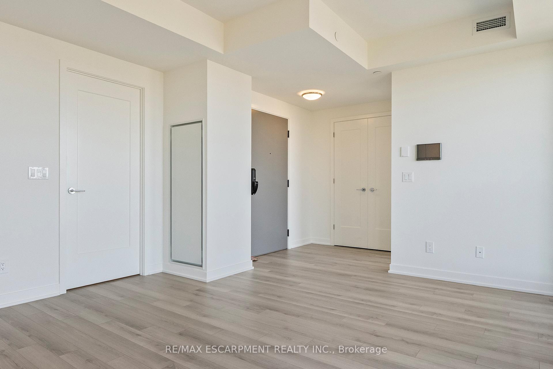Vacant condo entry foyer with light wood-look flooring, a mirrored panel, and double closet doors.
