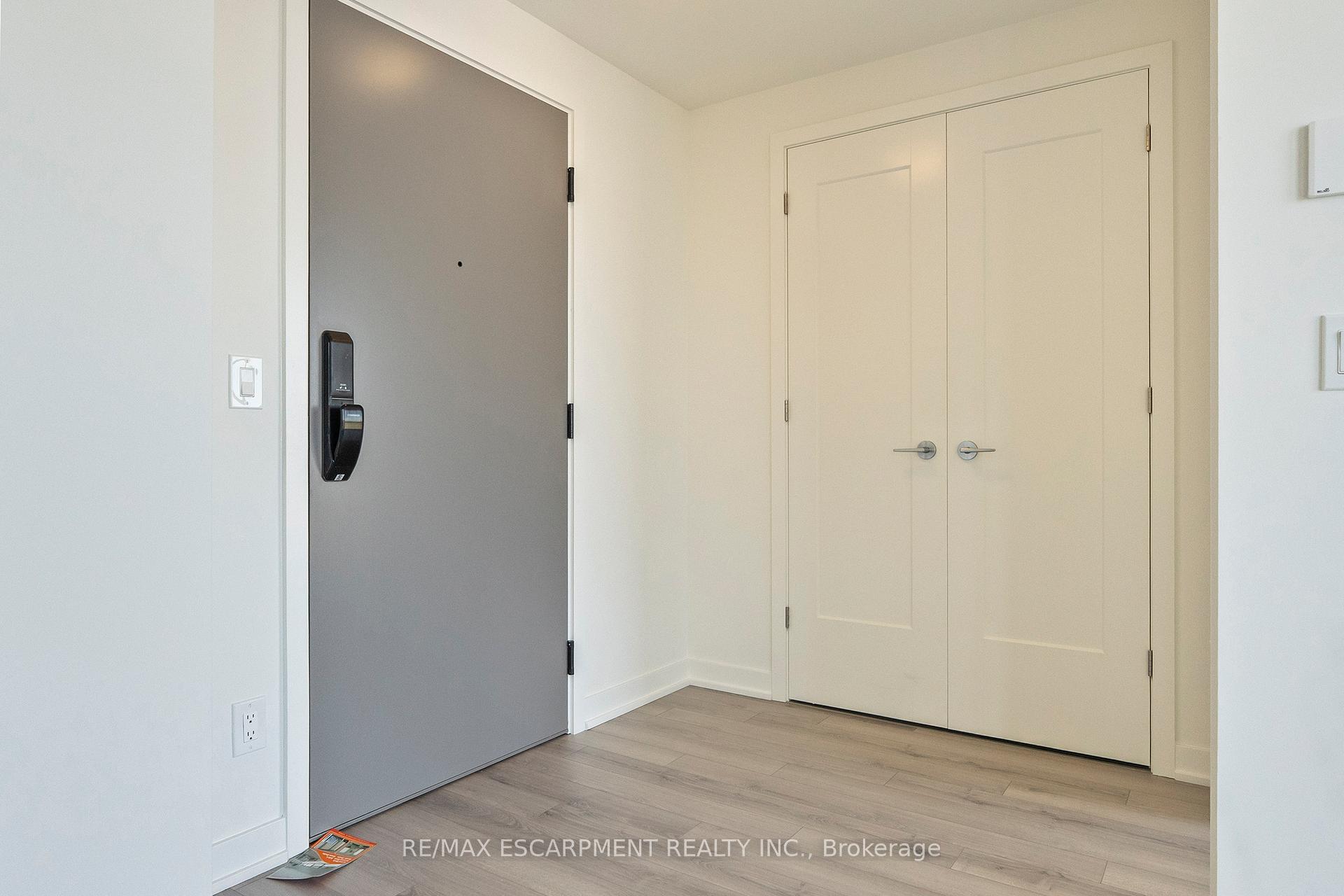 Condo entryway with a gray digital-lock front door, white double closet doors, and light wood-look flooring.