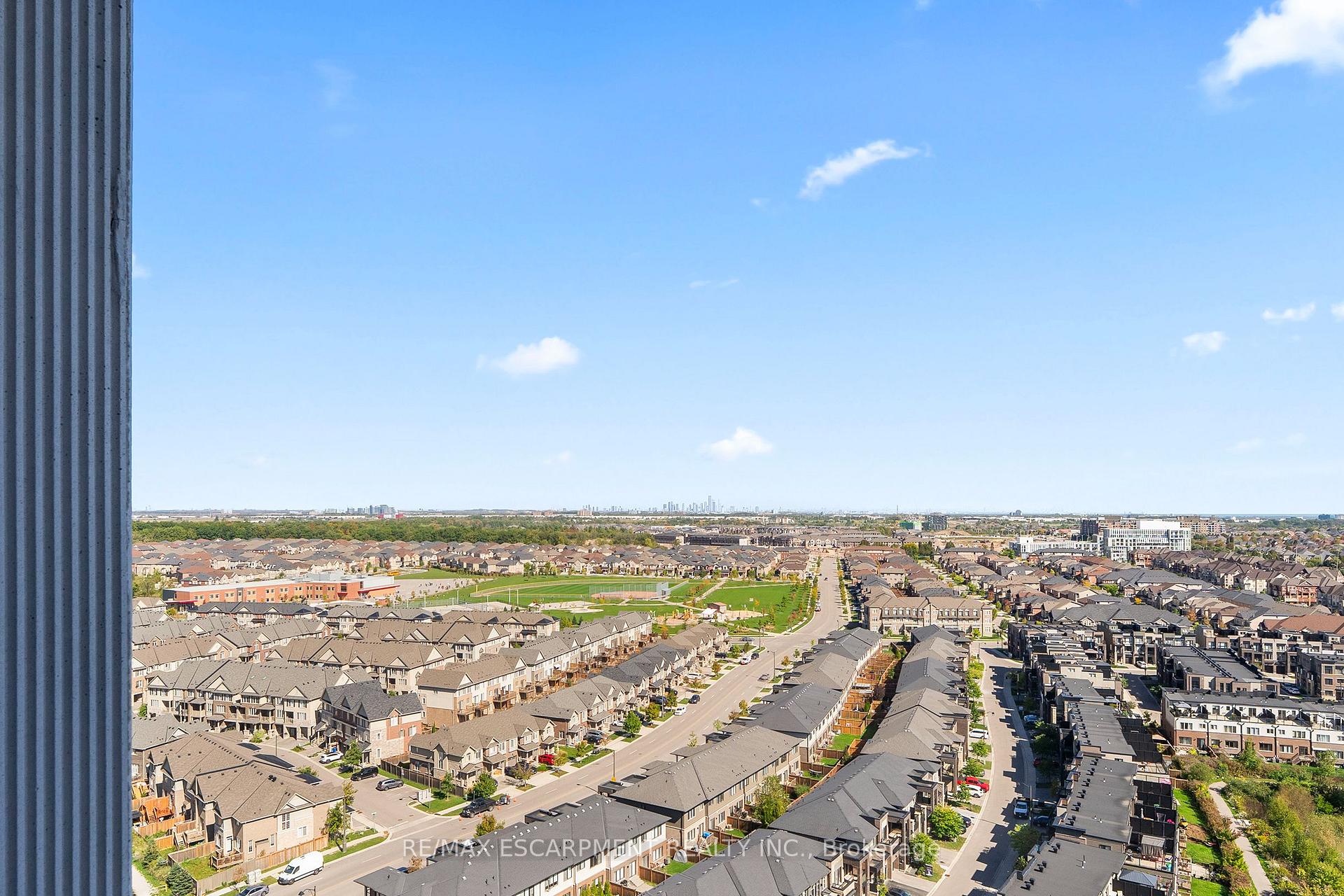 Elevated view over suburban homes and a park, with a distant skyline and a residential road below.