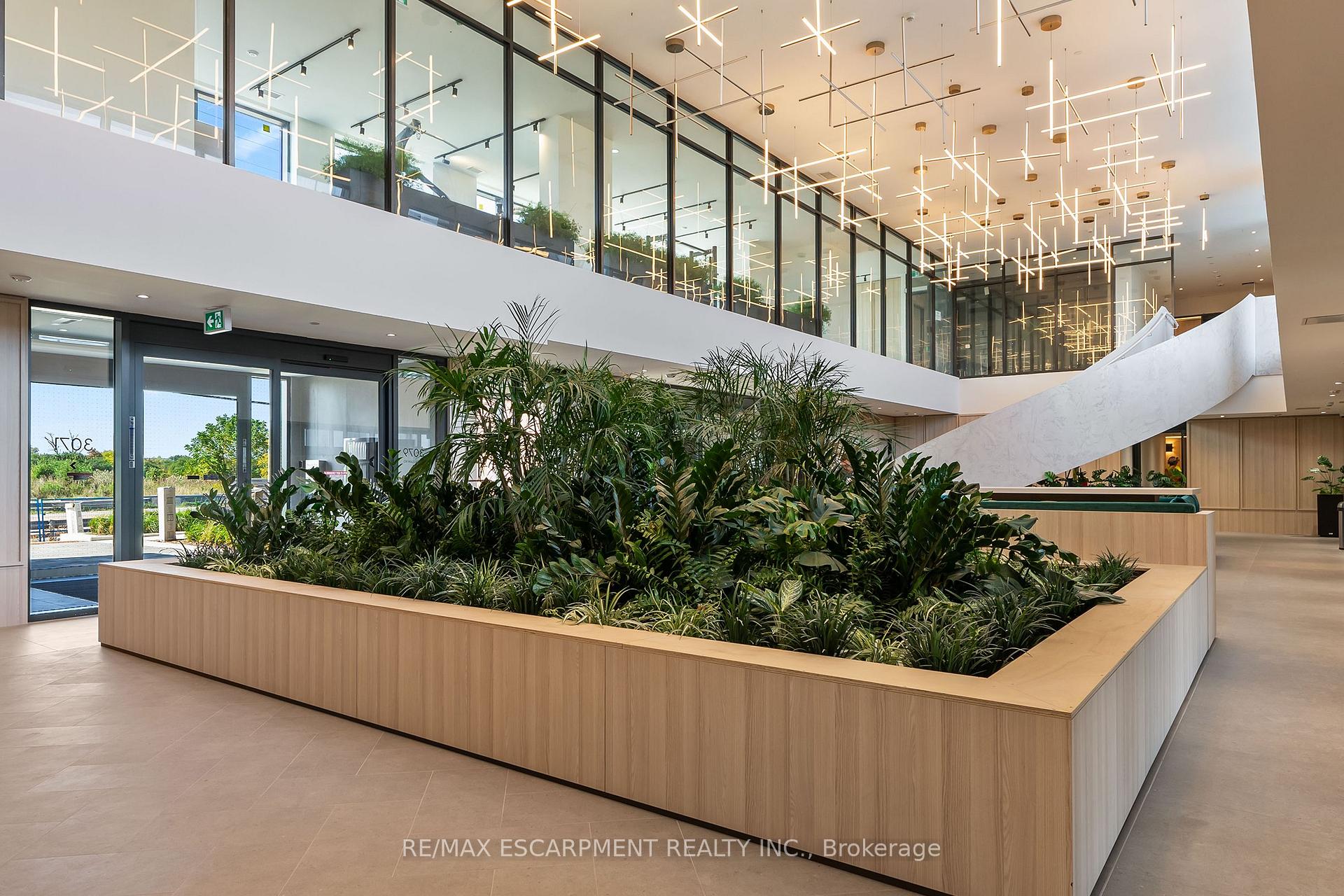 Modern condo lobby with a lush built-in planter, sweeping staircase, and geometric pendant lights.