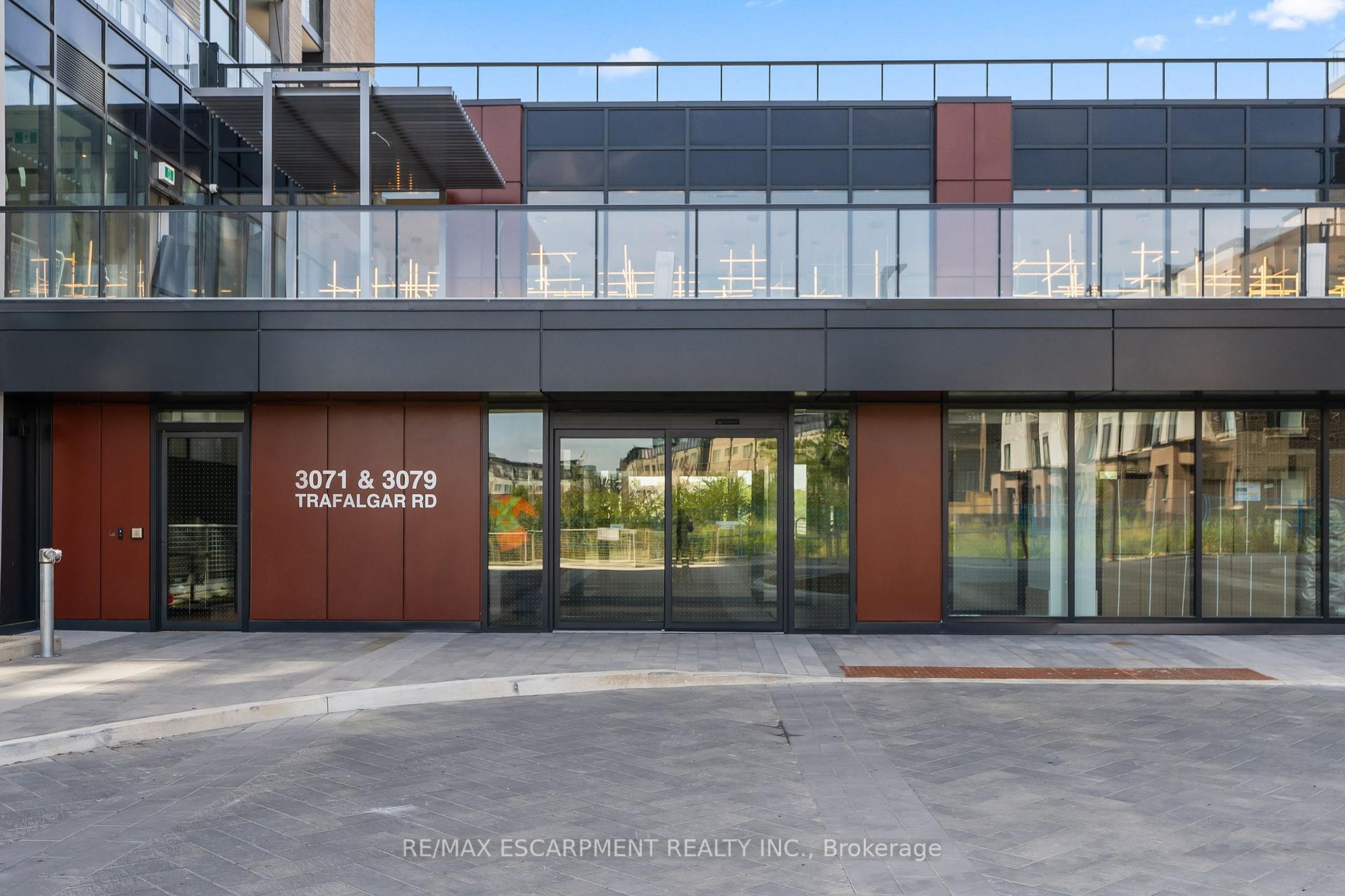 Modern Trafalgar Road building entrance with rust-colored panels, glass doors, and a paved forecourt.