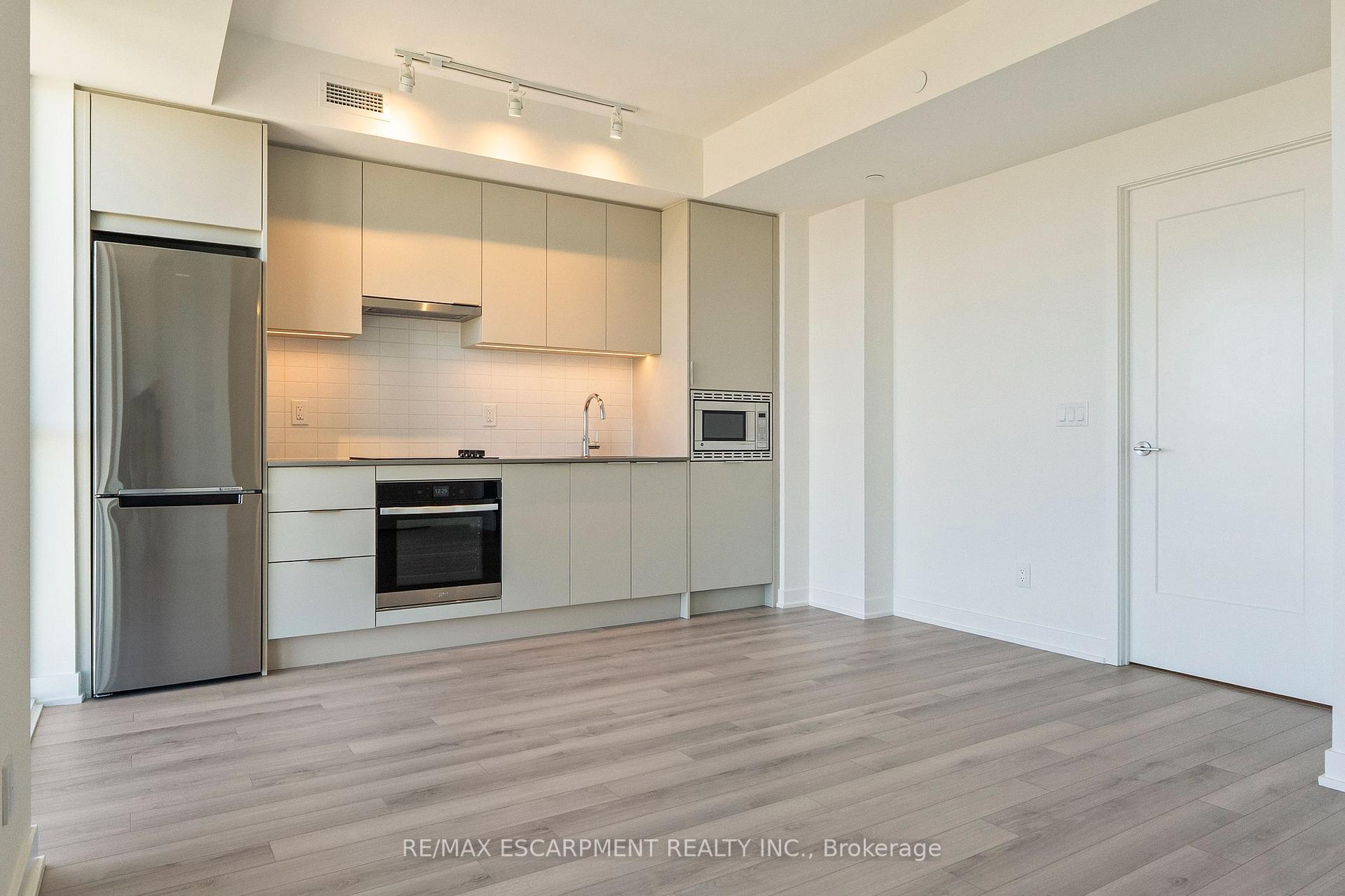 Vacant condo kitchen with pale cabinetry, stainless steel appliances, and light wood flooring.