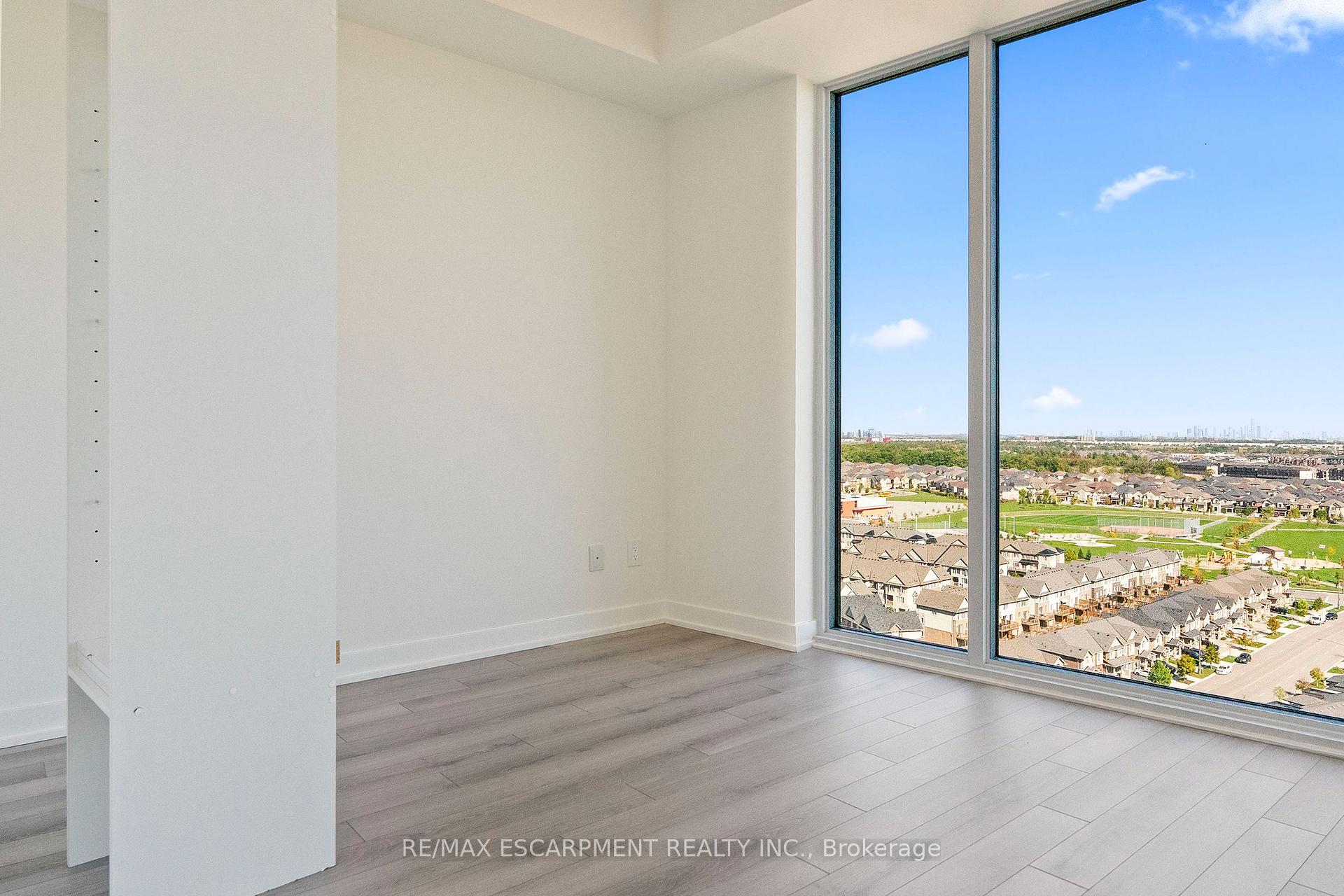 Vacant condo room with floor-to-ceiling windows overlooking homes and green space.
