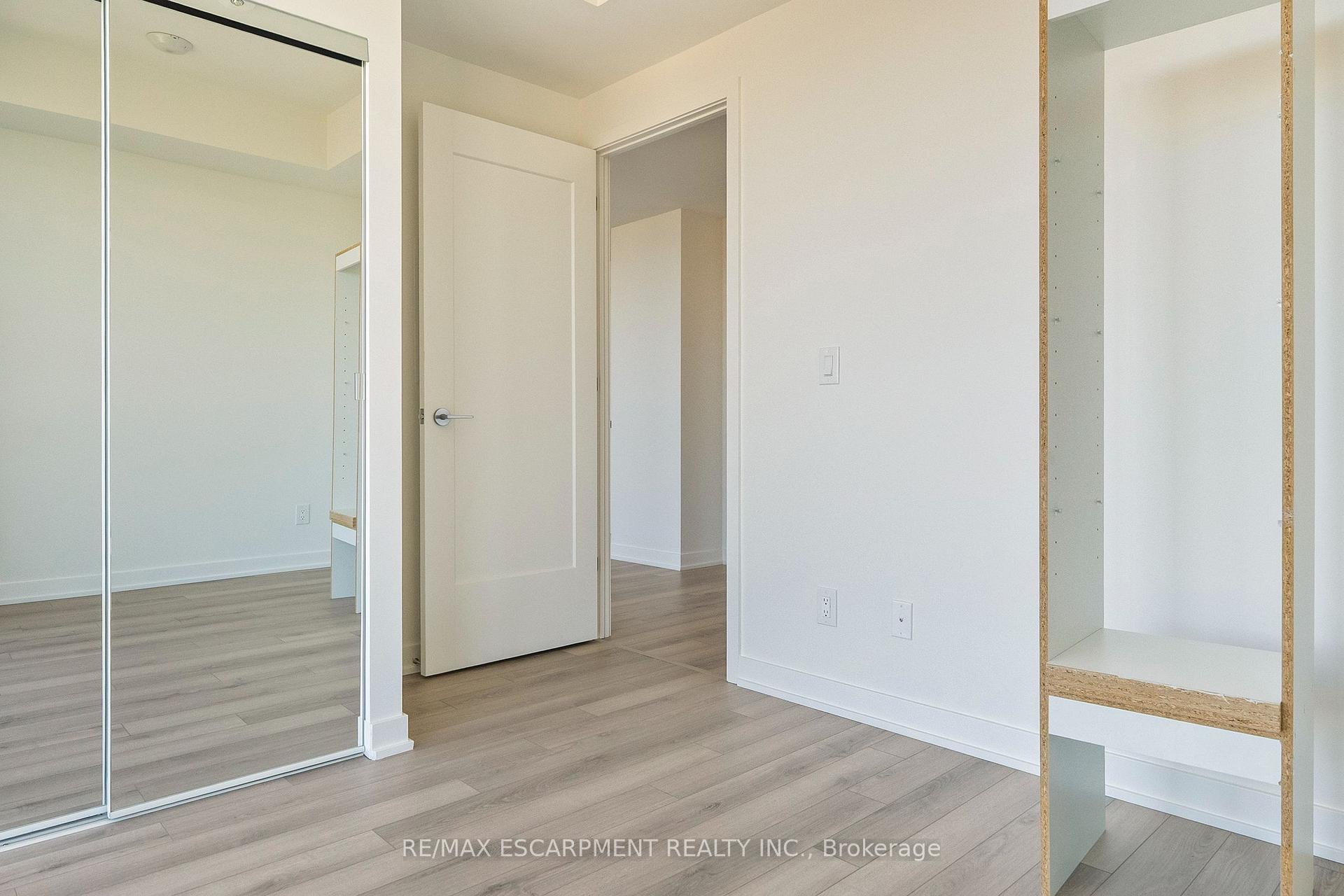 Empty bedroom with mirrored closet doors, open shelving, and light wood-look flooring.