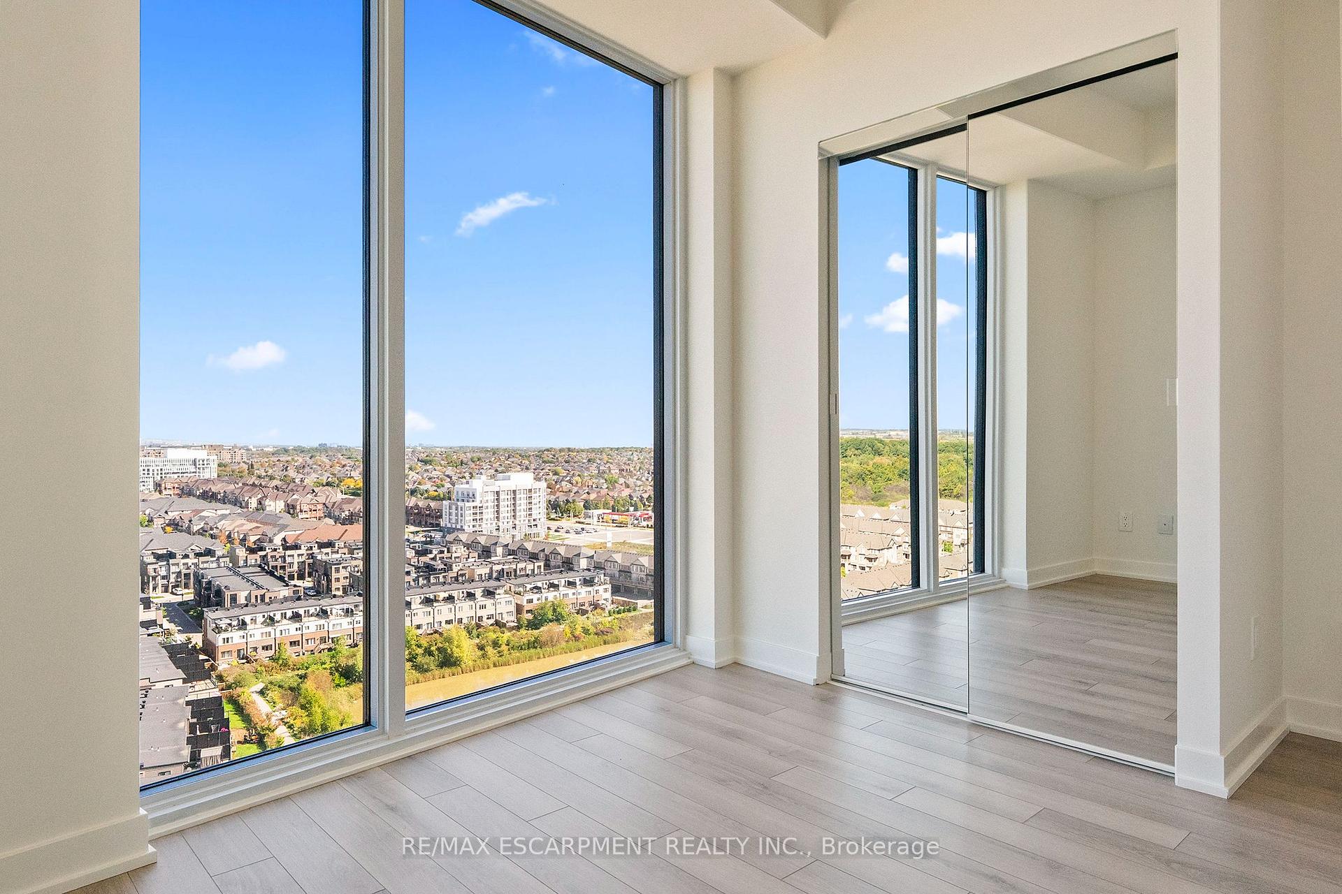 Empty high-rise room with floor-to-ceiling windows overlooking suburban rooftops and mirrored closet doors.