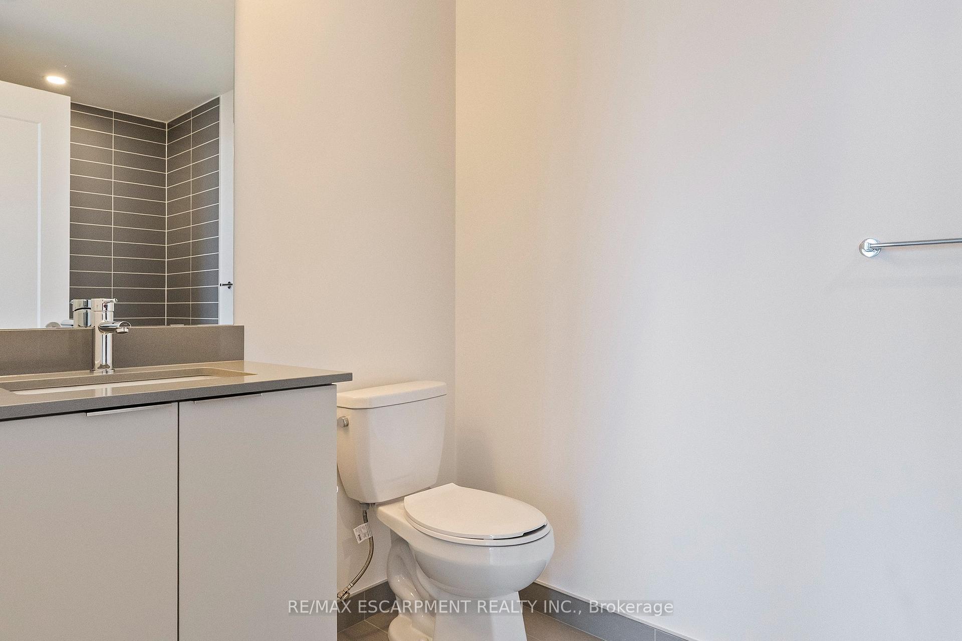 Modern bathroom with a white vanity, gray countertop, toilet, and dark horizontal wall tile.