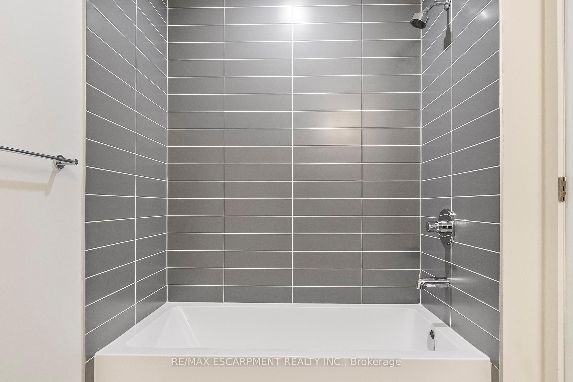 Gray-tiled bathtub and shower with chrome fixtures.