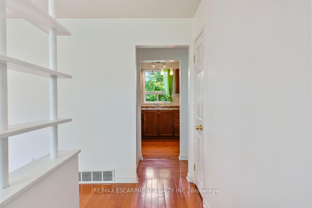 Empty hallway with built-in white shelves and hardwood floors leading to a kitchen.