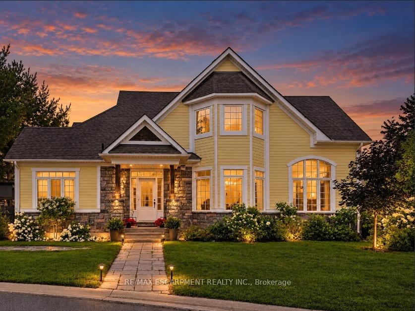 Two-story yellow house with stone accents and illuminated windows at dusk.