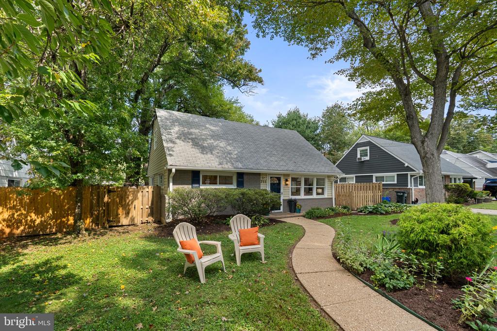 Gray-sided home with a steep roof, curved front walkway, mature trees, and two lawn chairs.