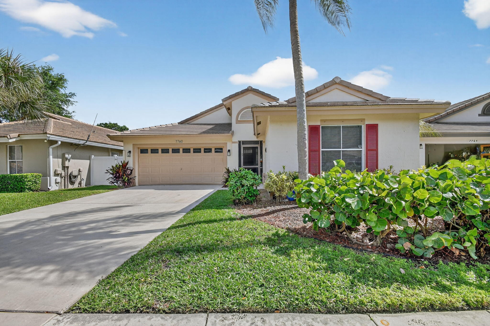 Home exterior with tan double garage, red shutters, palm tree, and landscaped front yard.