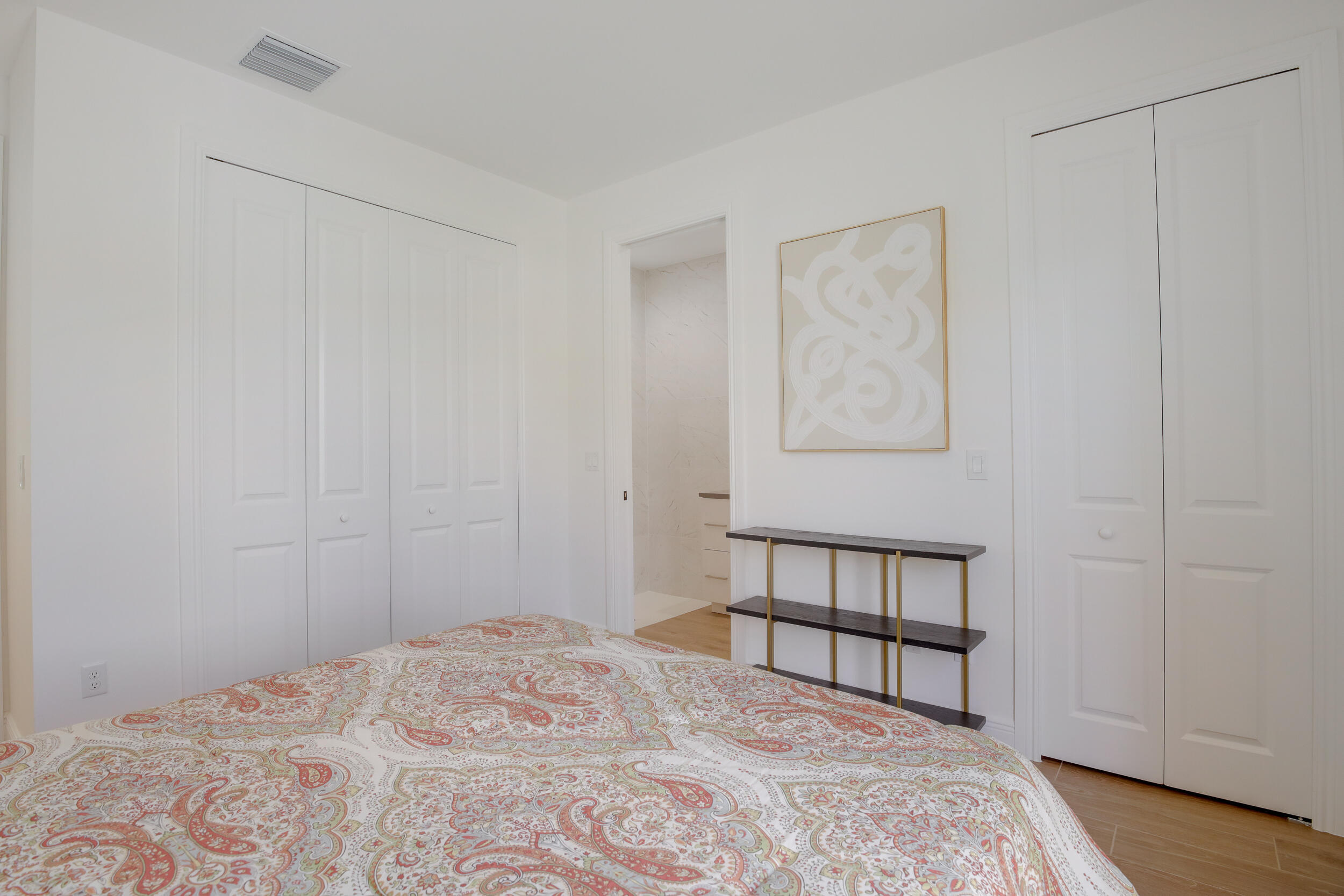 Bedroom with coral paisley bedding, white closets, and an open doorway to a marble-finished bathroom.