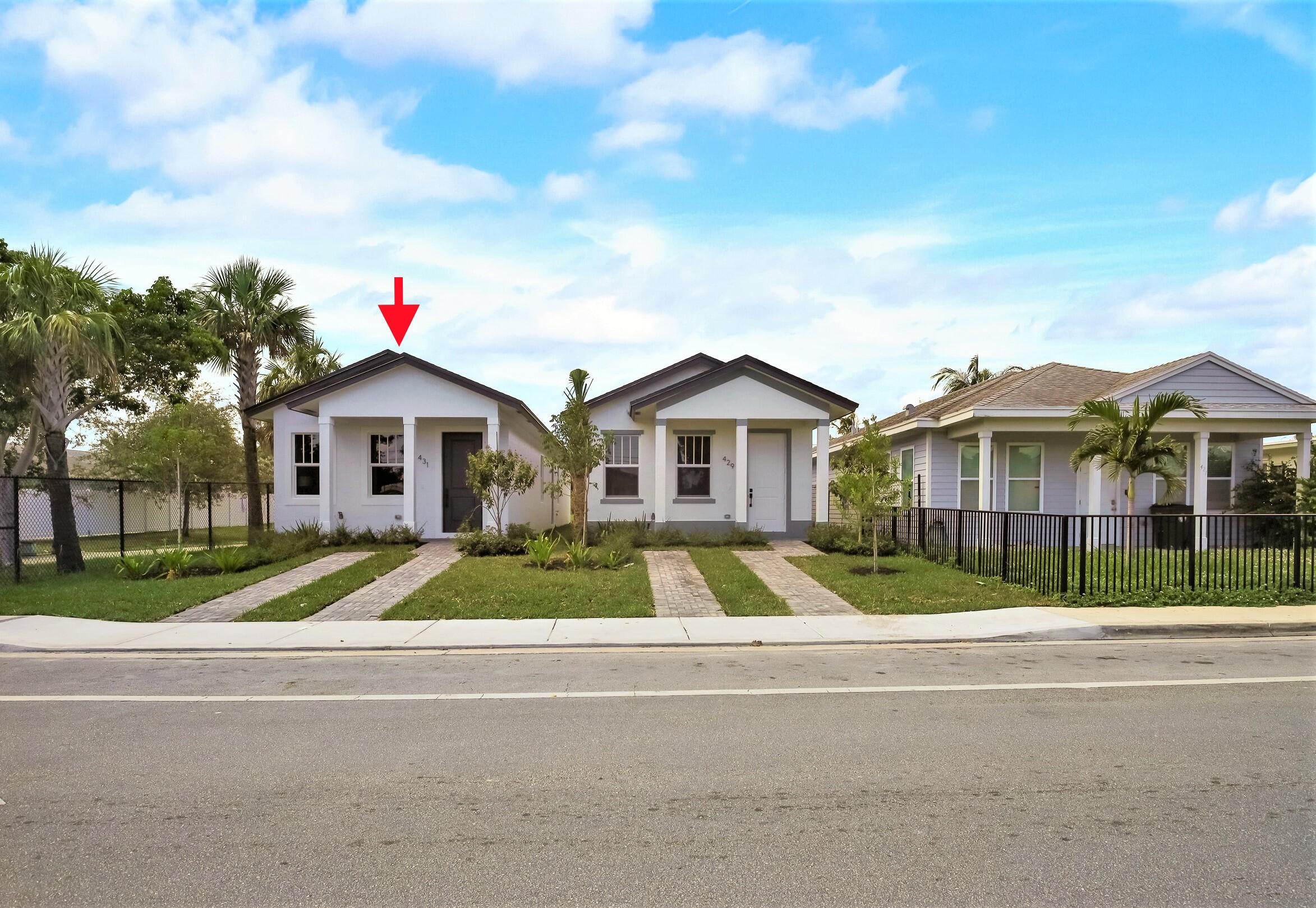 White single-story home with a dark gabled roof, landscaped lawn, and red arrow marking it.