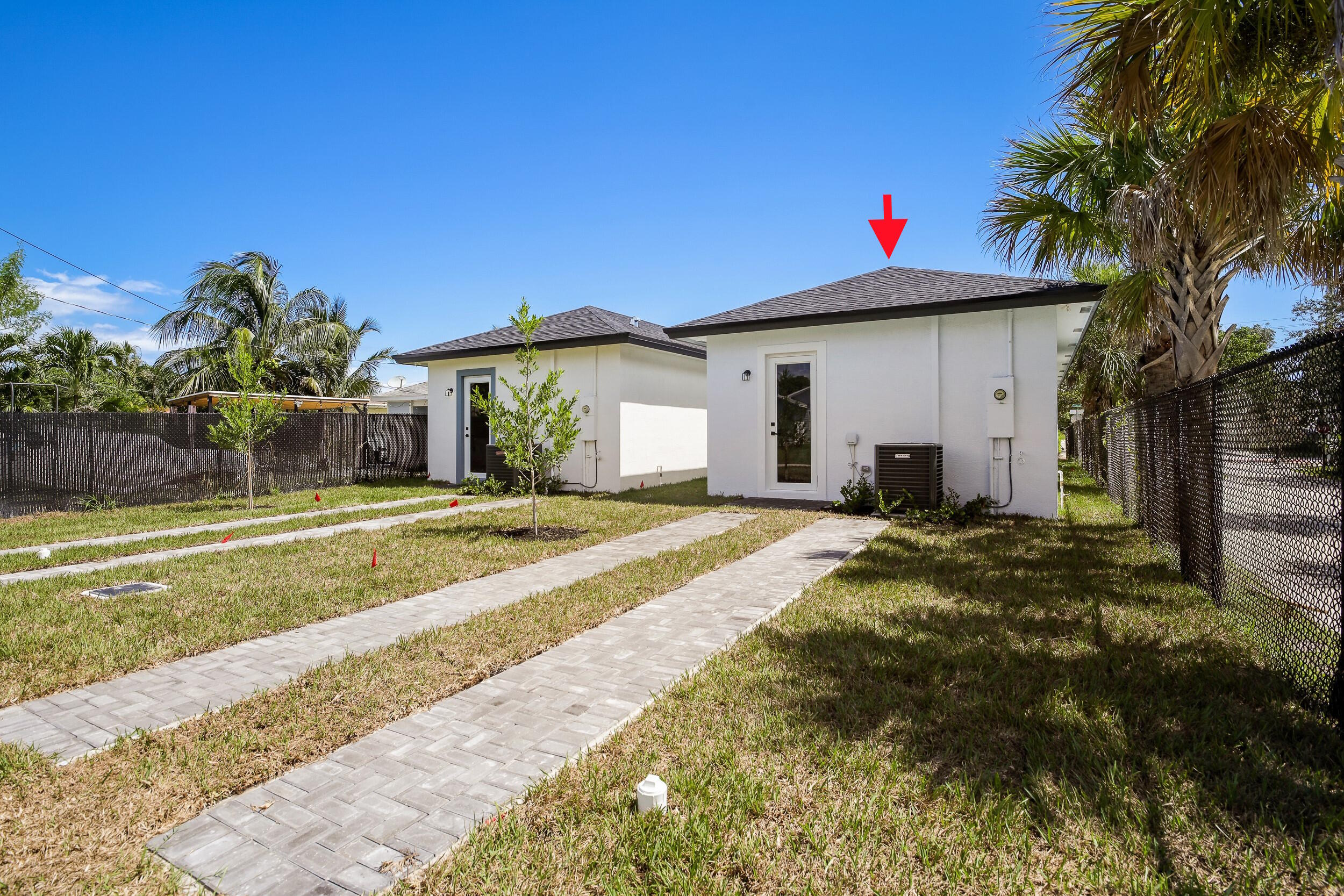 White building marked by a red arrow, beside a smaller building and paved walkways.