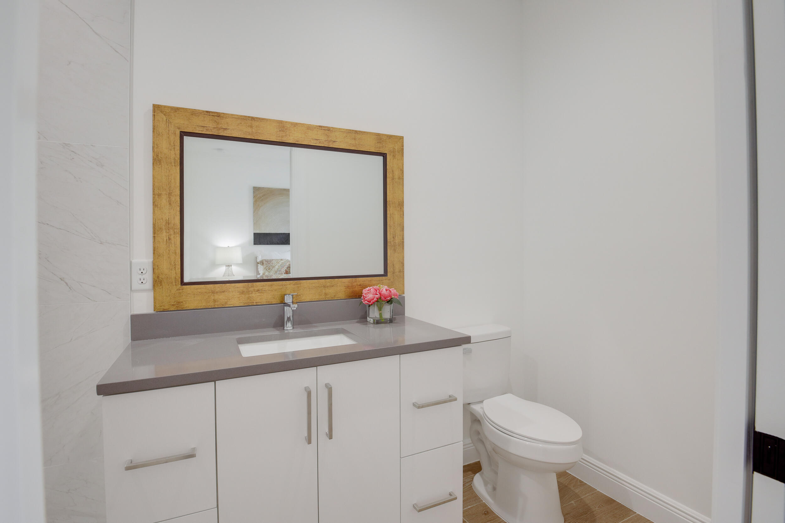 Modern bathroom vanity with a wide wood-framed mirror, taupe counter, and white toilet.
