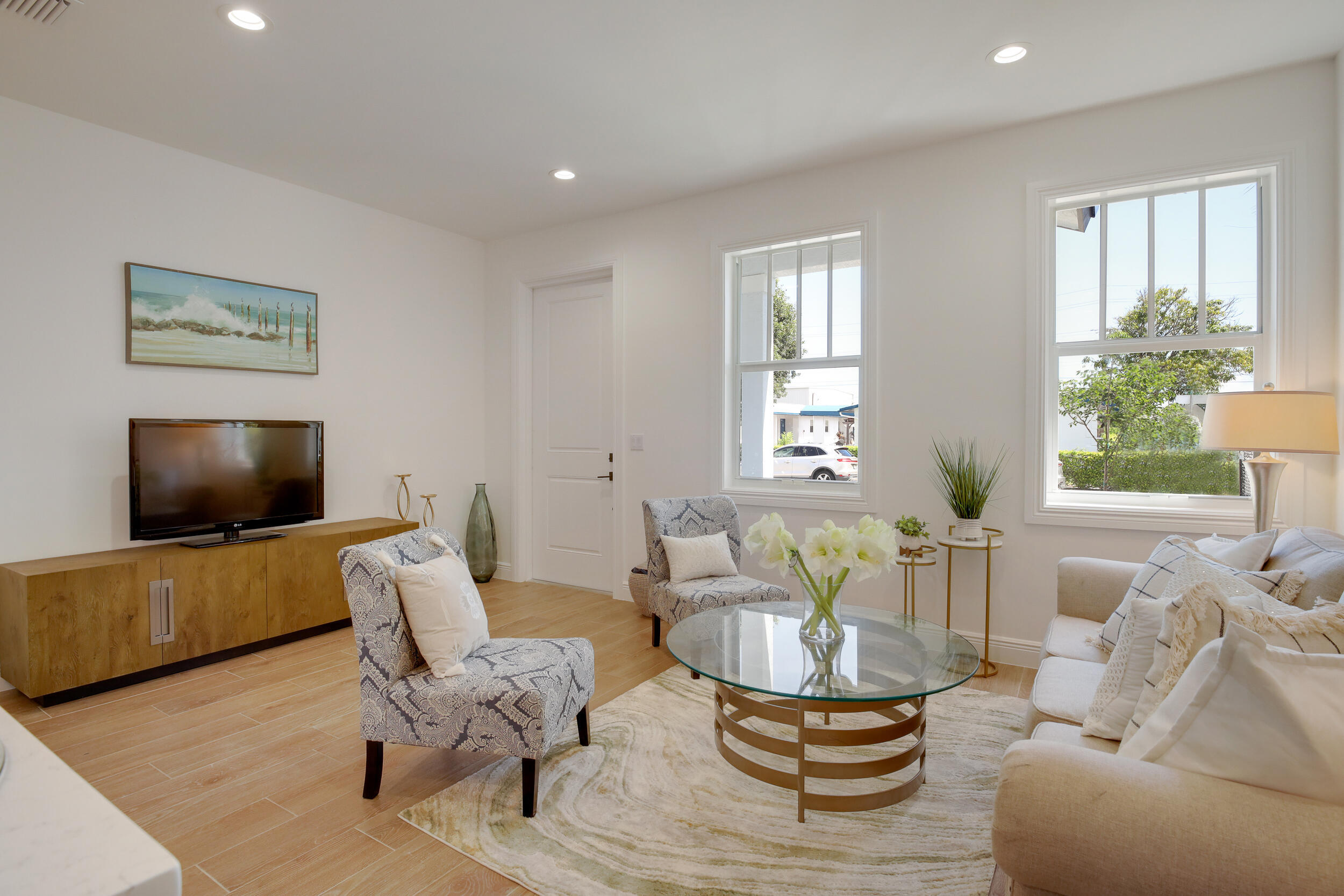 Furnished living room with large windows, a white sofa, patterned chairs, and a glass coffee table.