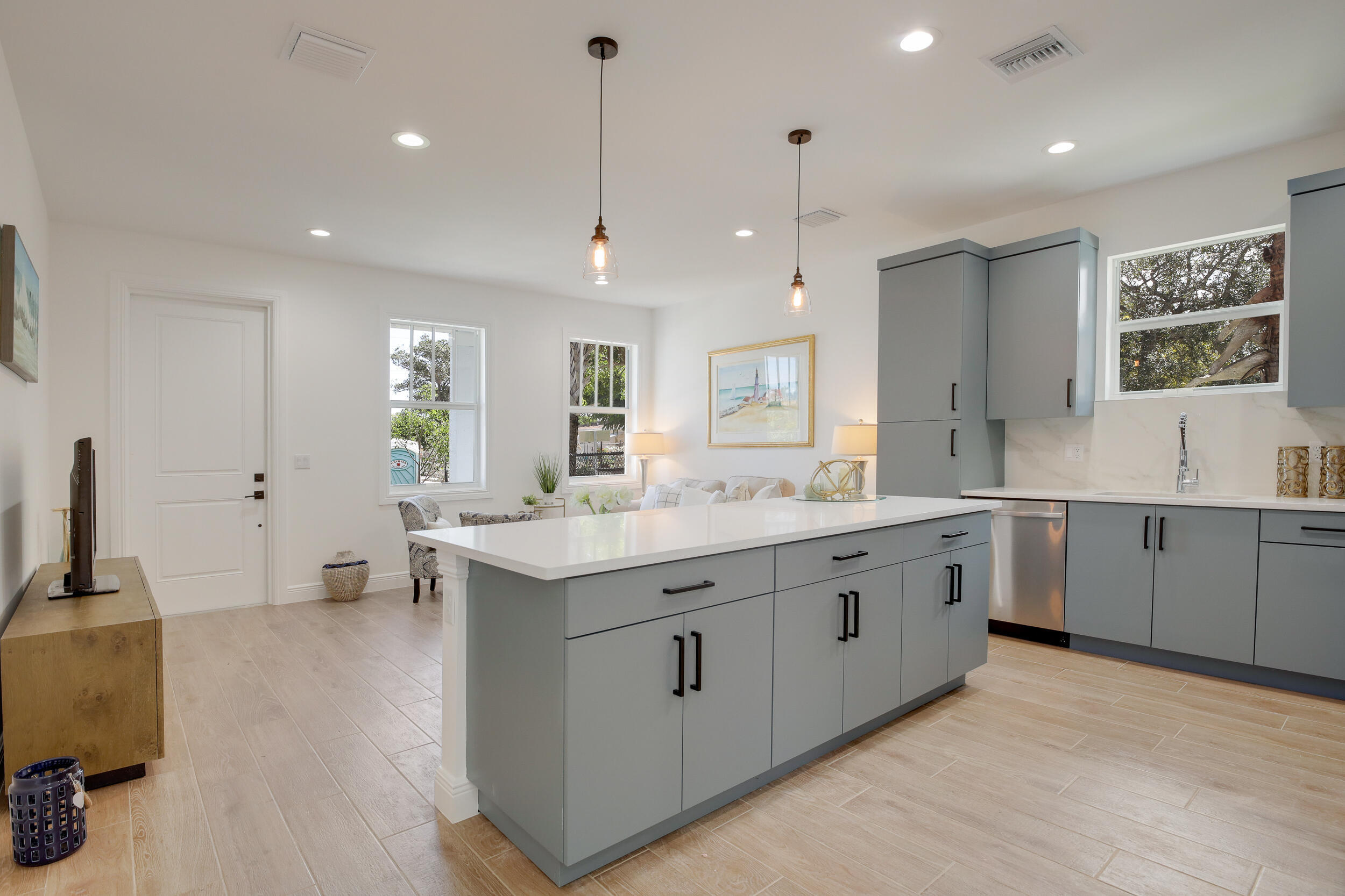 Bright open-plan kitchen with a large gray island, white counters, and windows overlooking trees.