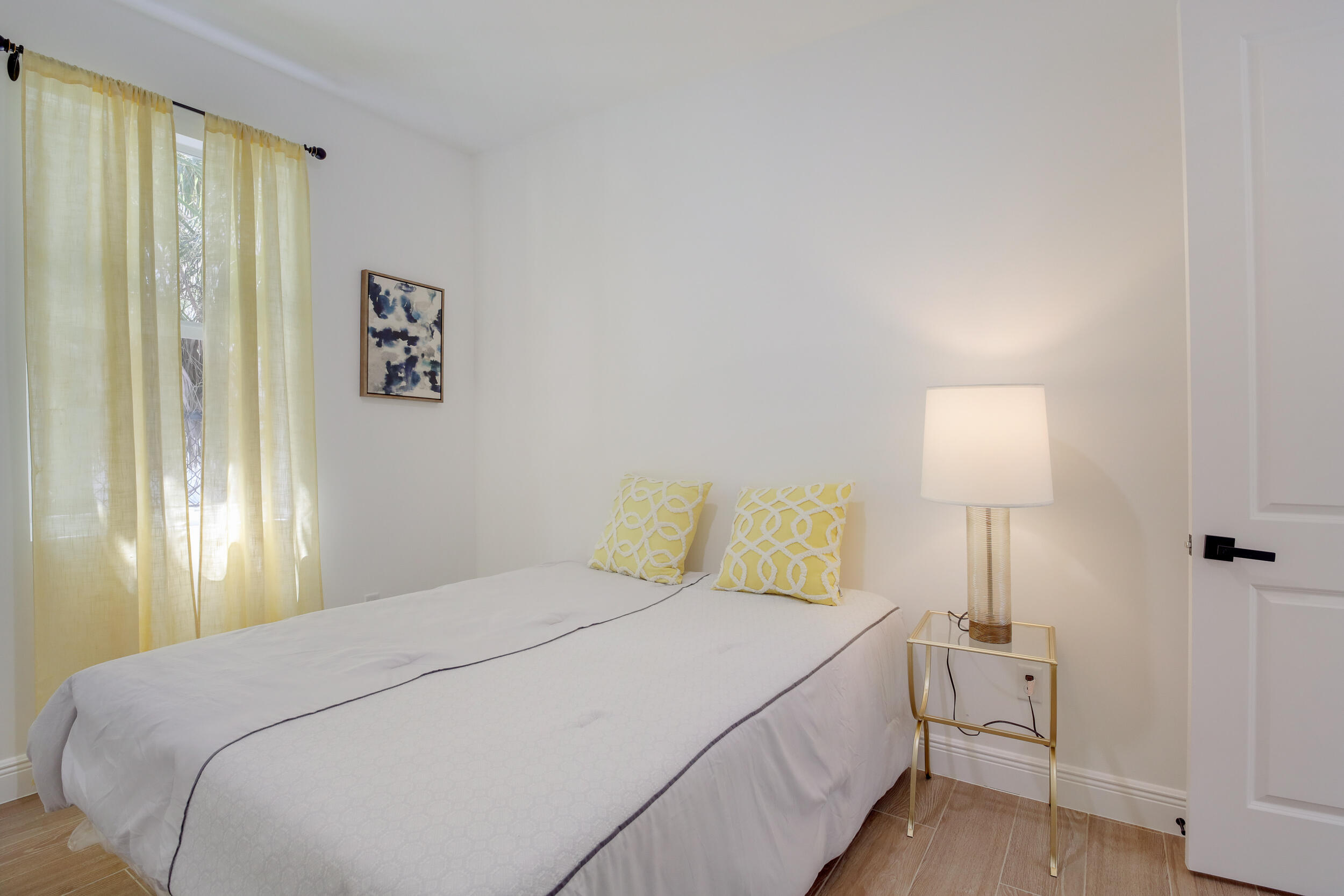 Furnished bedroom with yellow curtains and patterned pillows on a white bed.