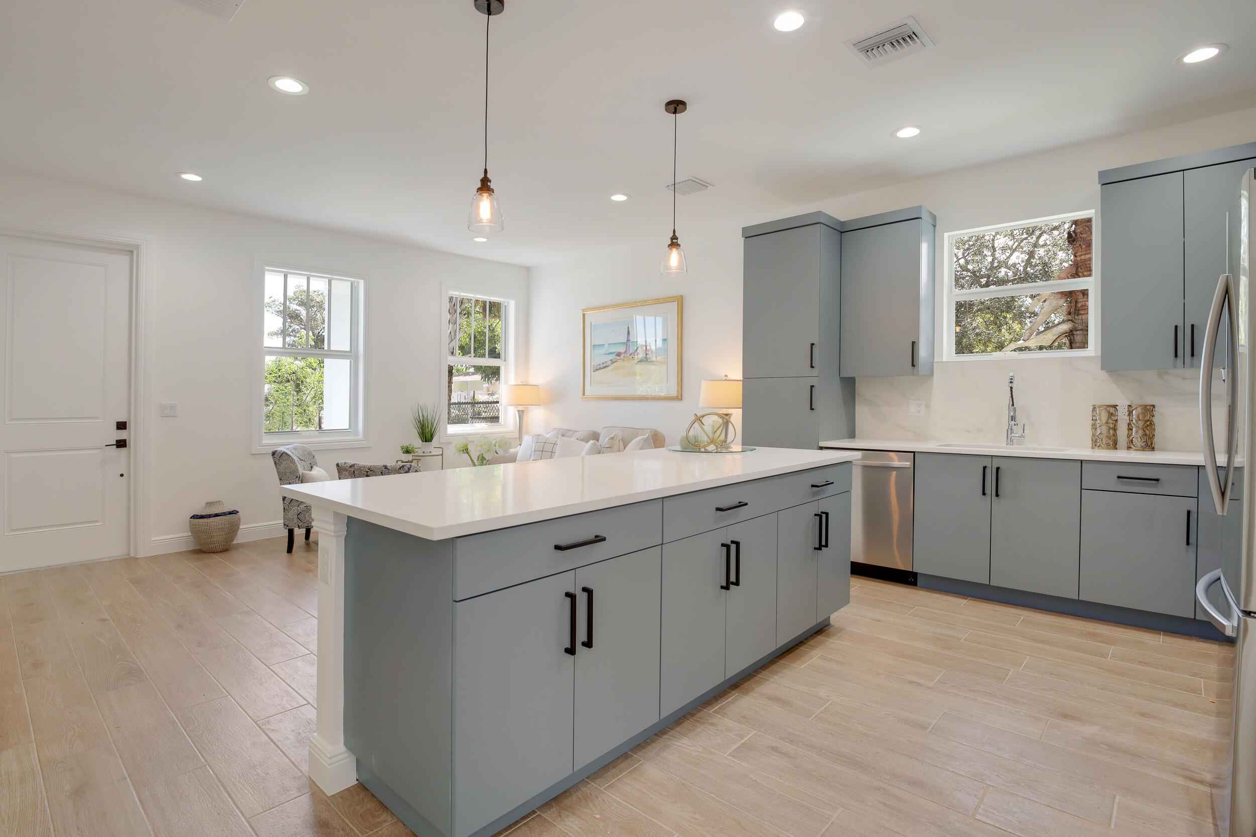 Renovated kitchen with gray cabinets, a large white island, and windows overlooking greenery.