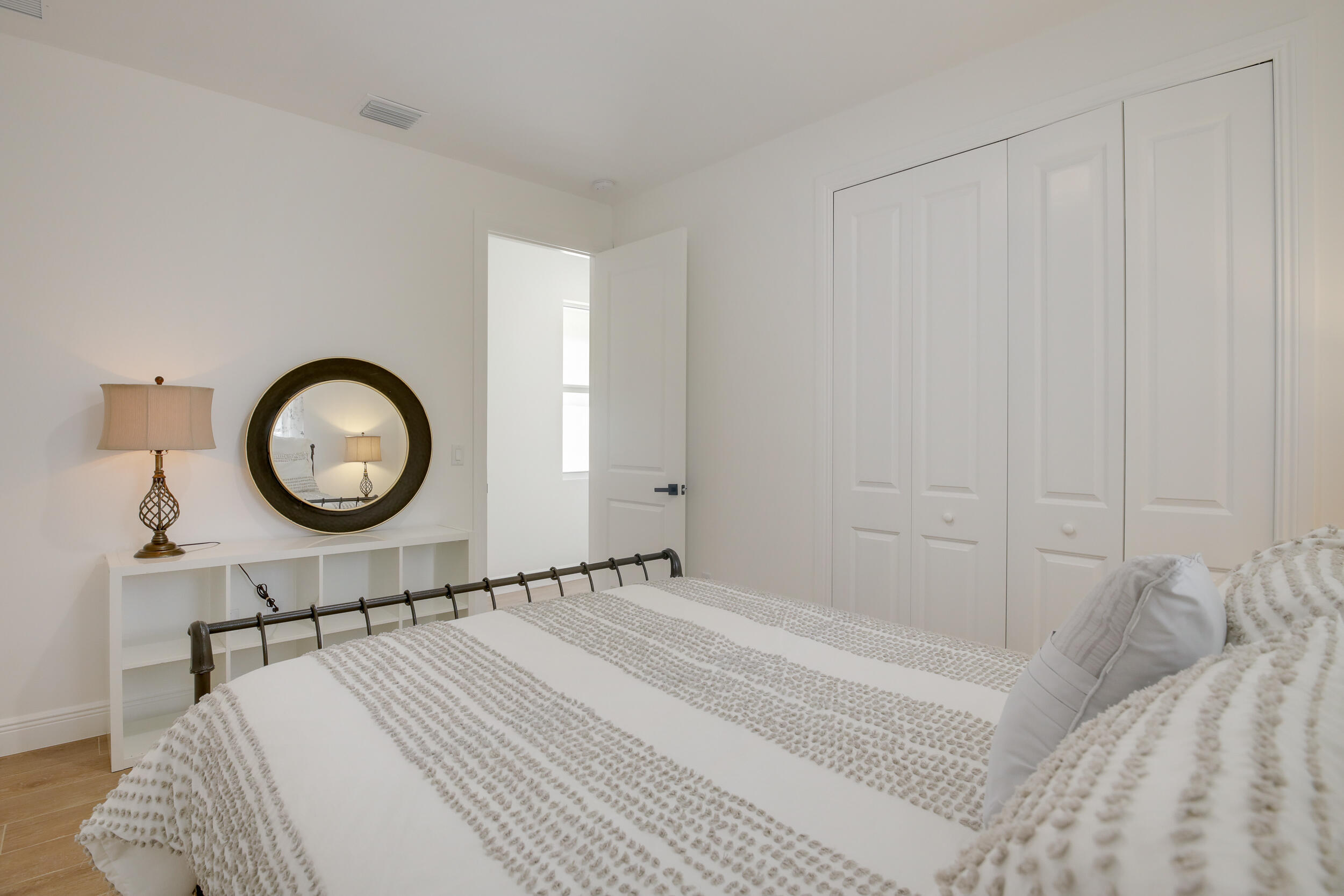 Bedroom with textured white bedding, a round mirror, and white closet doors.