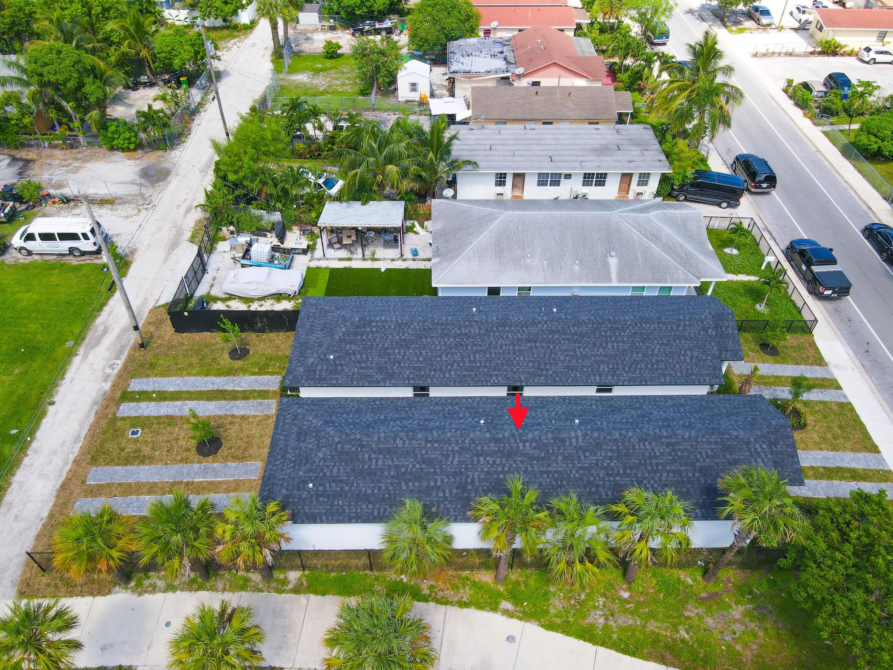 Aerial view of a low-rise property with dark shingle roofs, palm-lined frontage, and a red arrow.