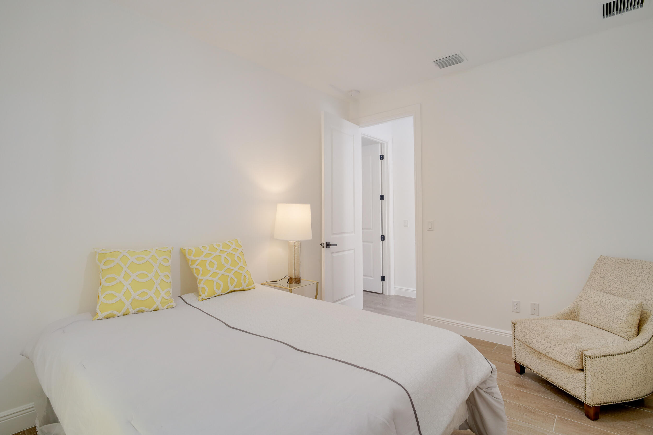 Staged bedroom with a white bed, yellow patterned pillows, and a cream armchair.