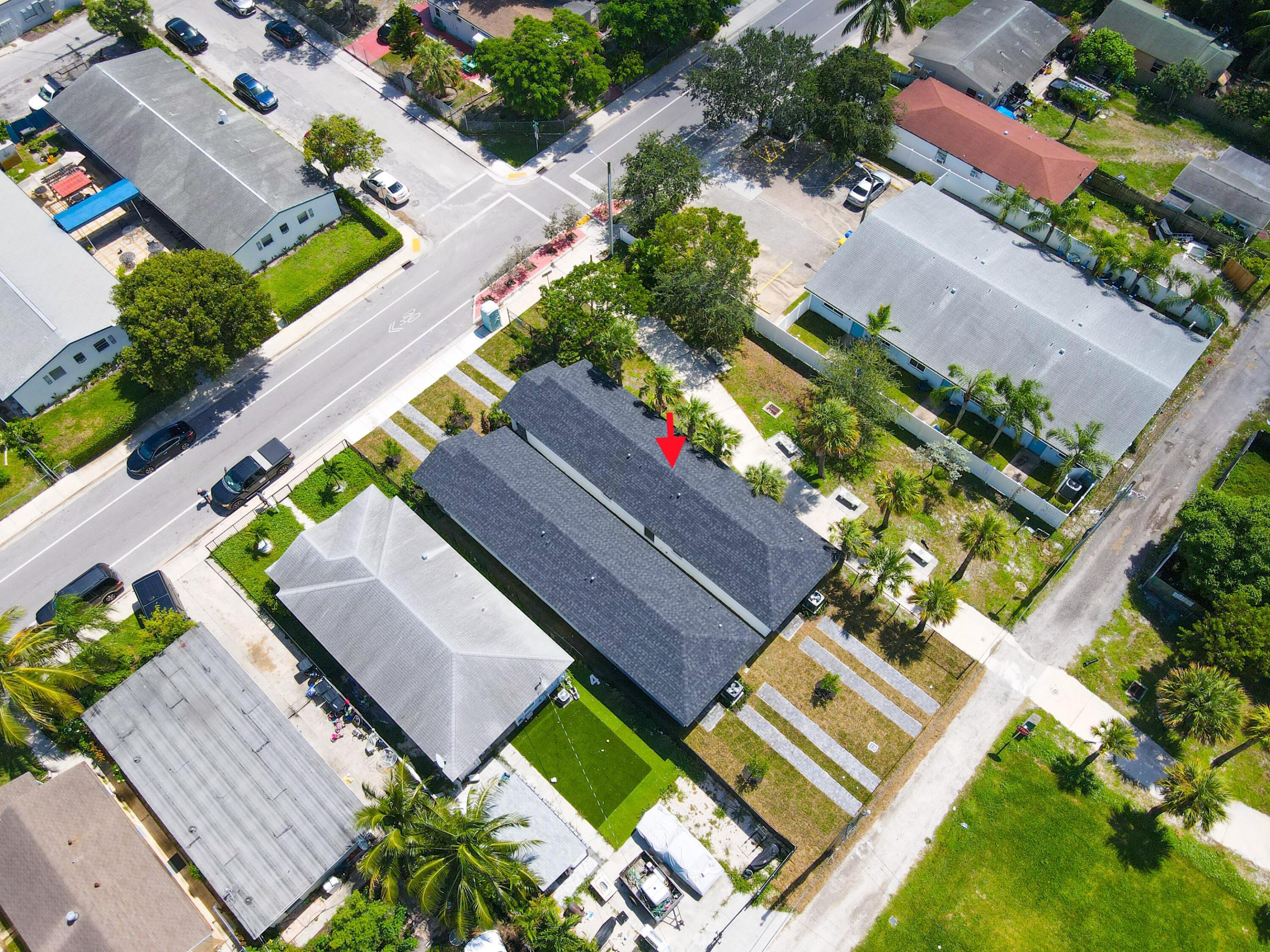 Aerial view of the dark-roofed home marked by a red arrow, surrounded by palm trees and neighboring houses.