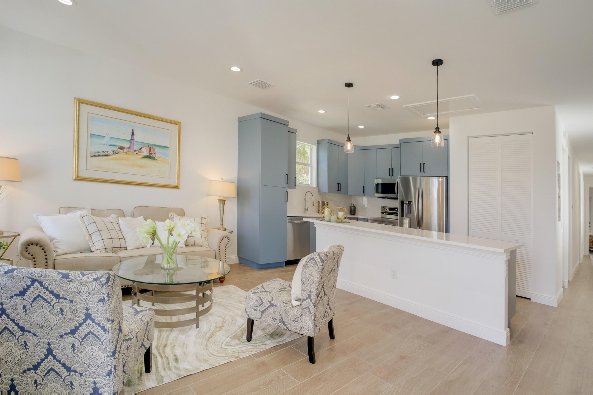 Open-plan living room and kitchen with blue-gray cabinets, stainless steel appliances, and patterned accent chairs.