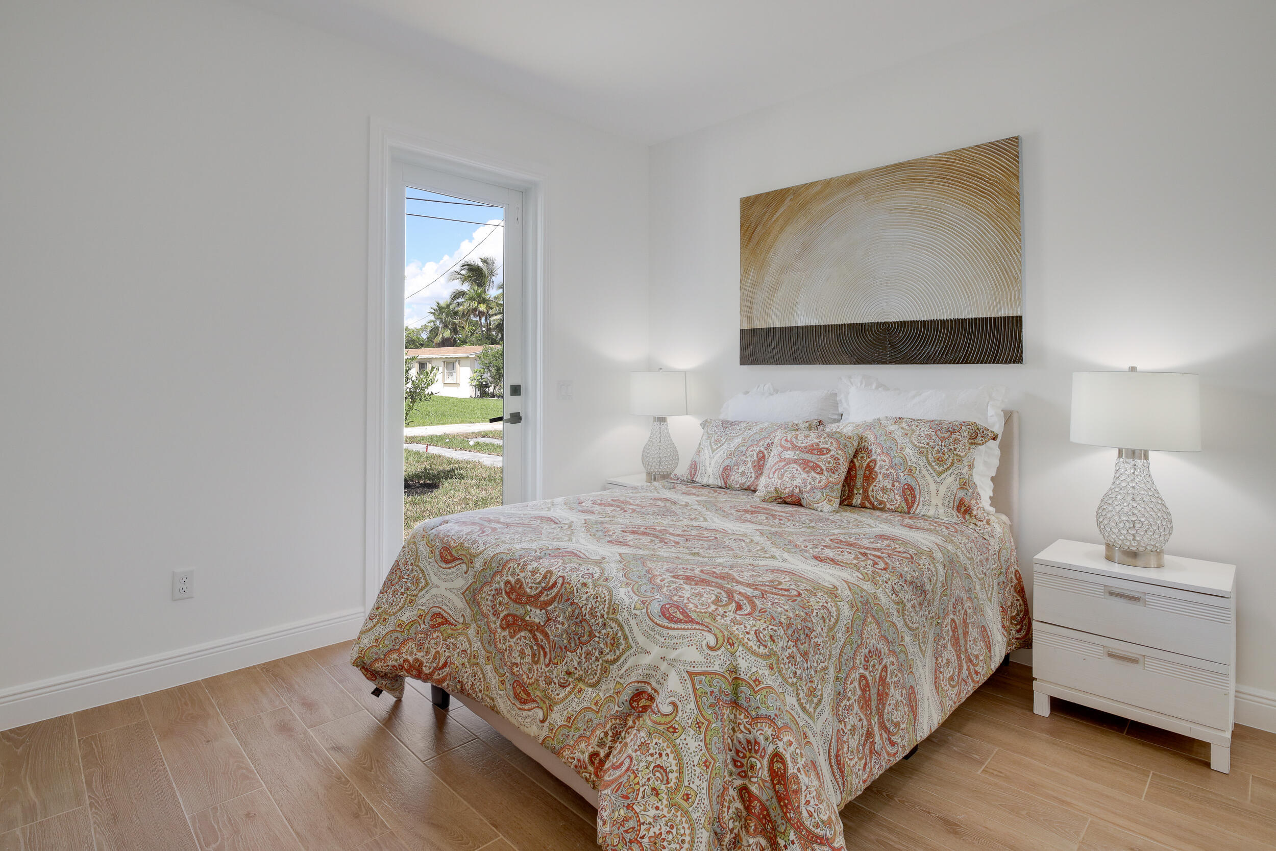 Bright bedroom with paisley bedding, matching bedside lamps, and a glass door overlooking palm trees.