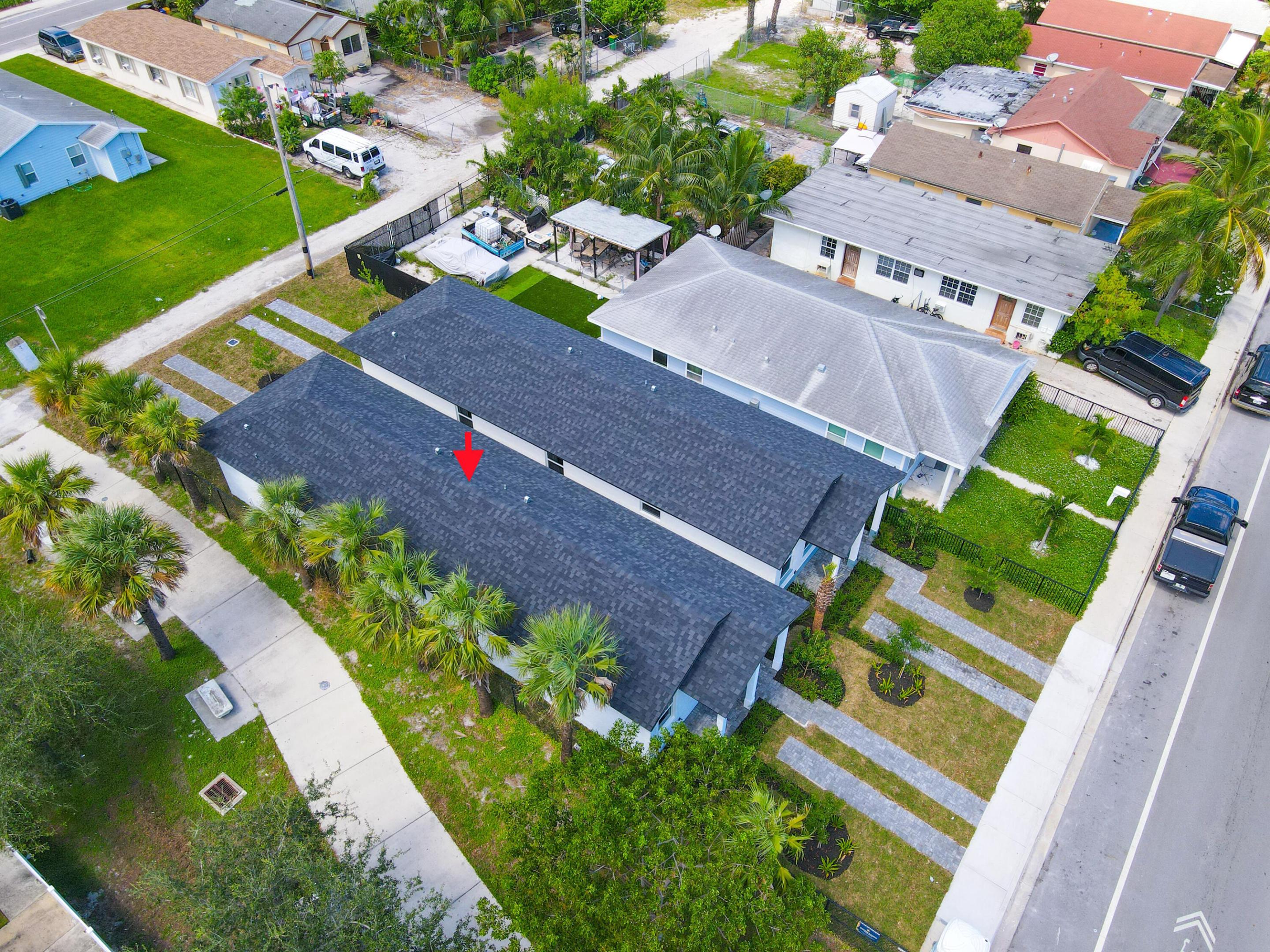 Aerial view of the arrow-marked home with dark shingle roofs, palm trees, and paved walkways.