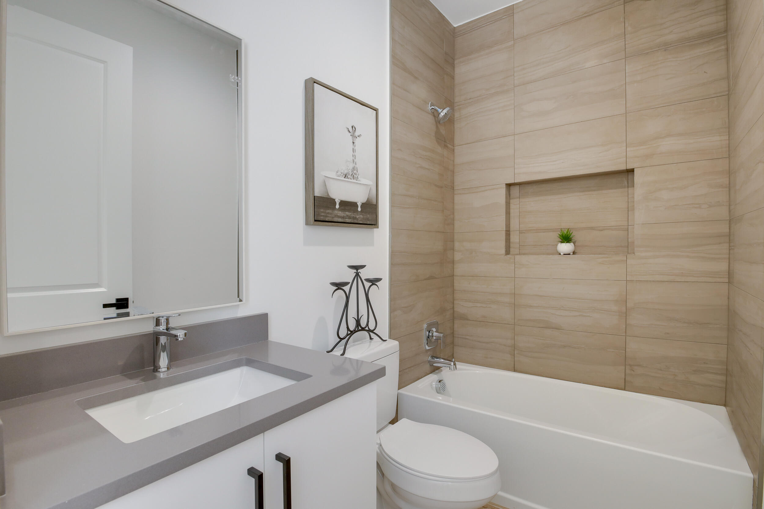 Bathroom with a gray vanity, white sink, and tub beneath beige tiled walls.