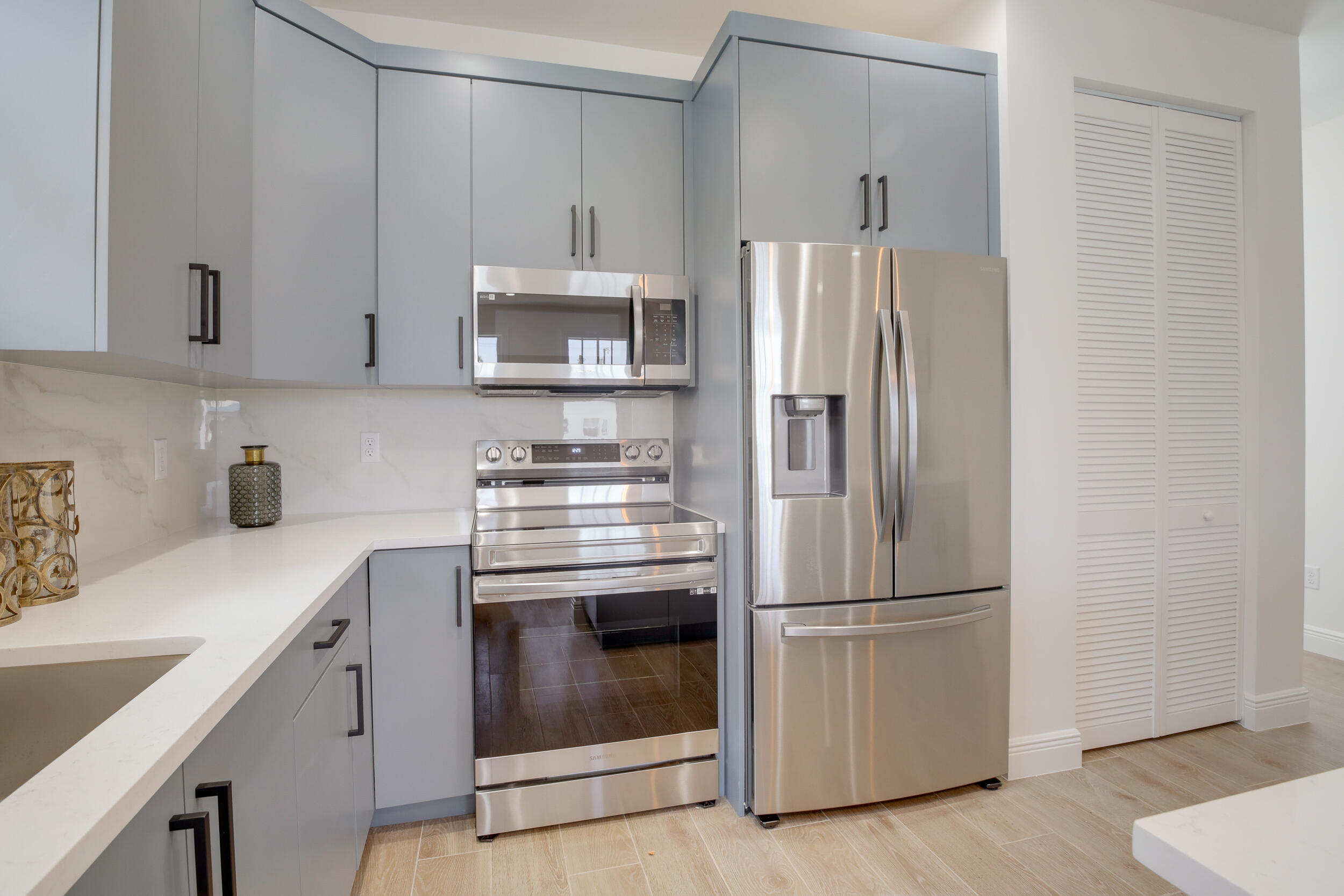 Modern kitchen with gray cabinets, white stone counters, and stainless steel appliances.