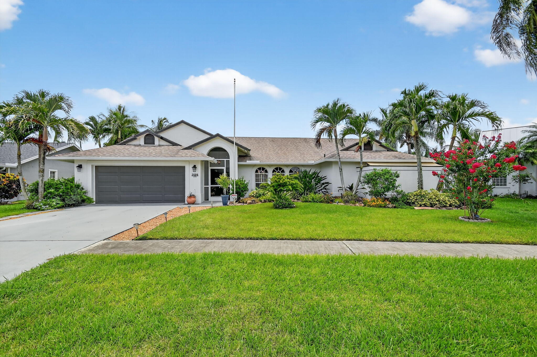 Single-story white house with a gray double garage, arched entry, palms, and a broad green lawn.