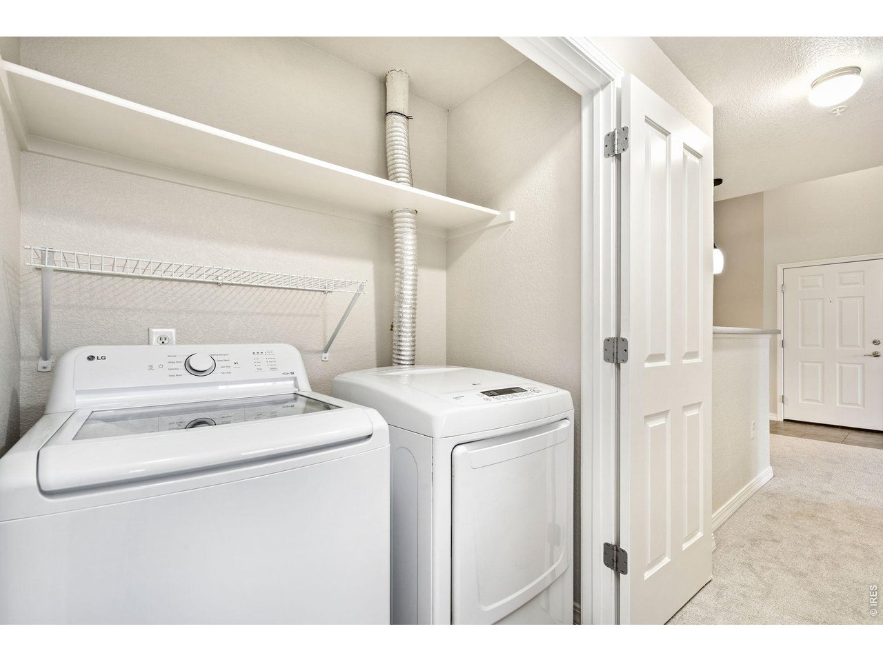 Laundry room with white washer and dryer beneath open shelving, viewed through the open doorway.