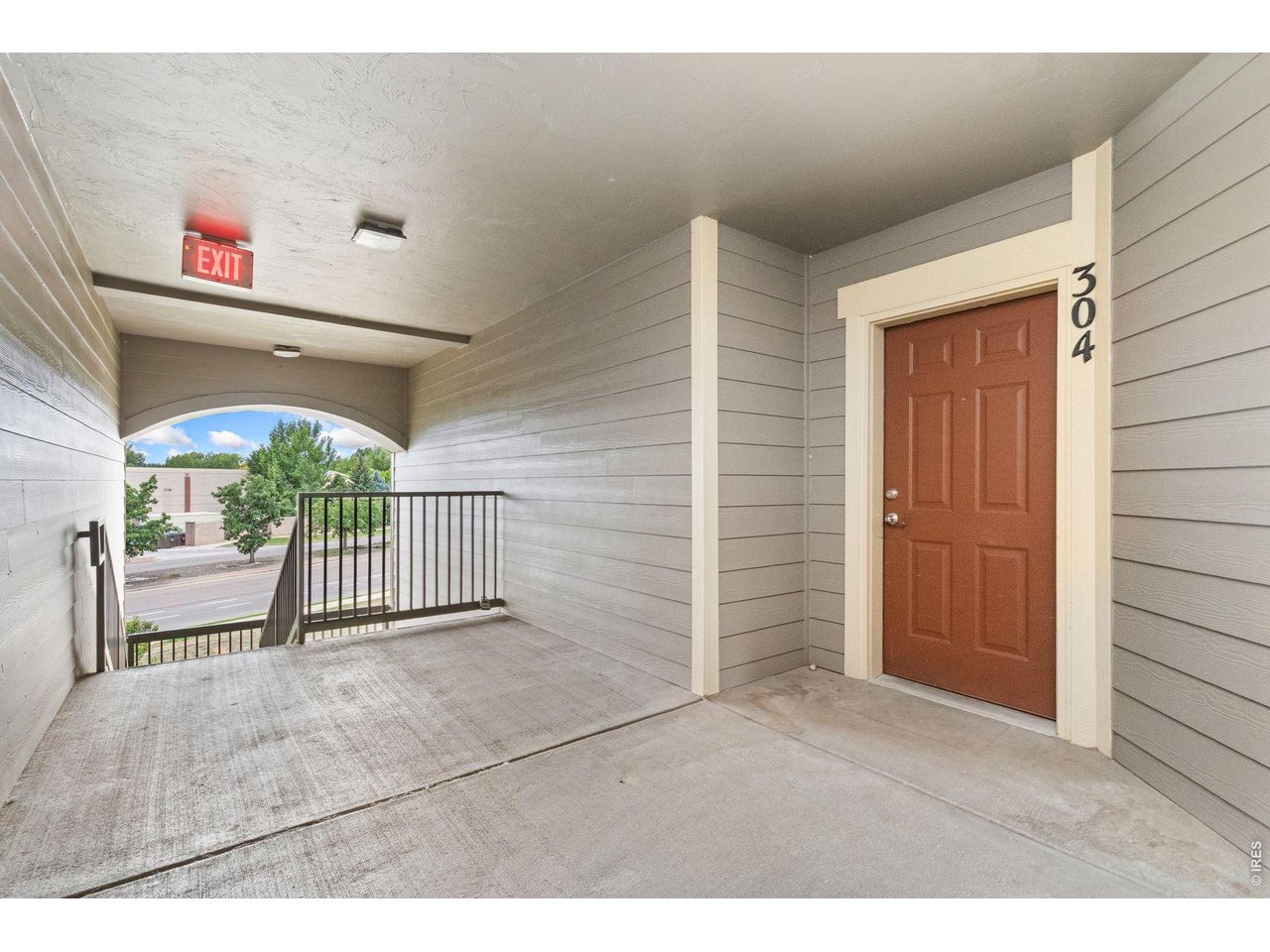 Covered apartment entry walkway with unit 304’s reddish-brown door and a black metal railing.