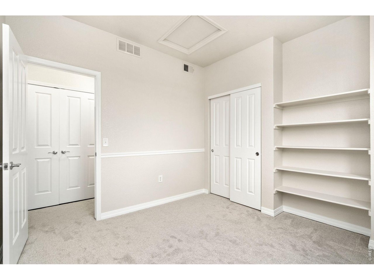 Empty carpeted room with white closet doors, built-in shelves, and an open doorway.