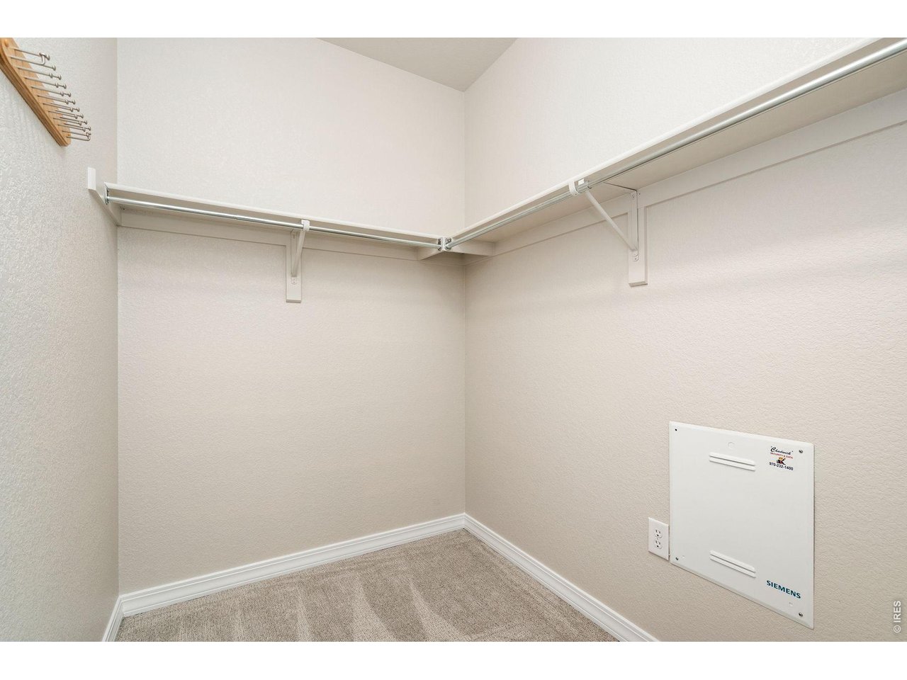 Empty walk-in closet with beige carpet and hanging rods and shelves along two walls.
