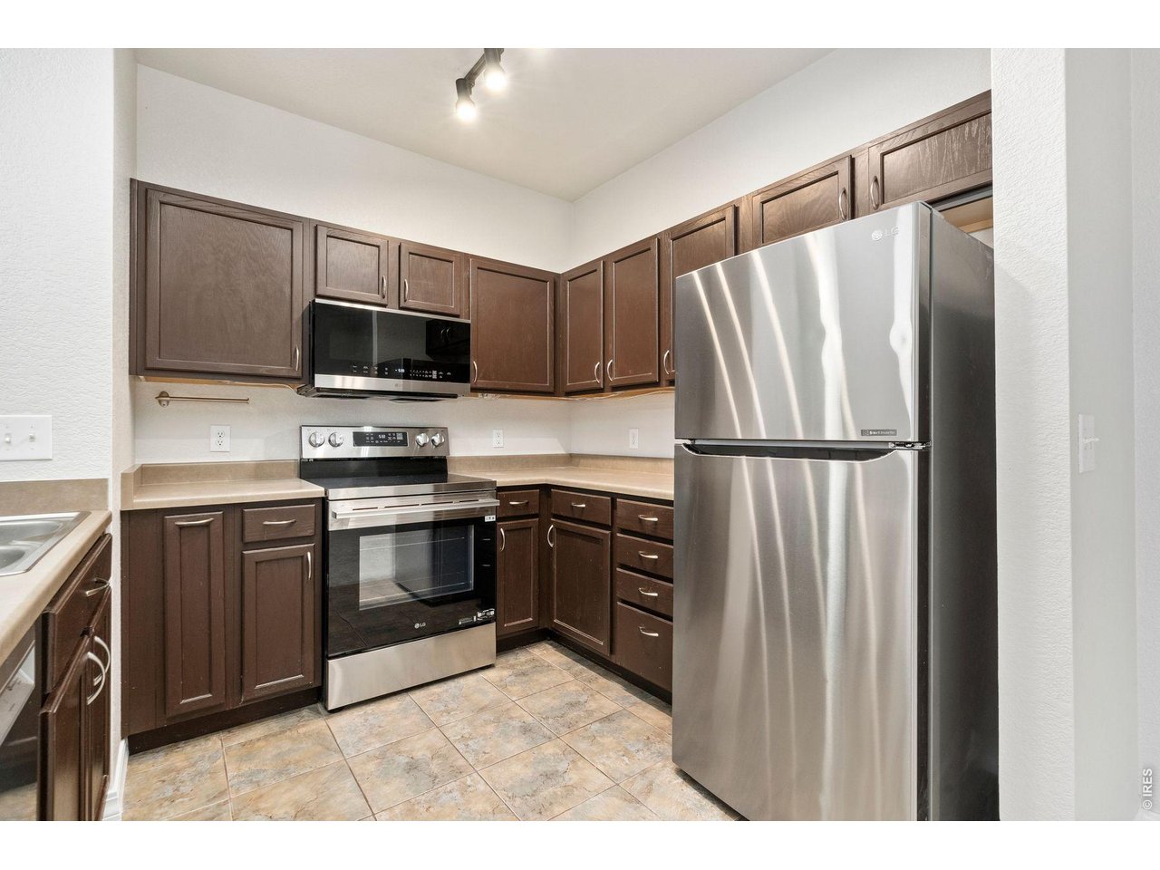 Kitchen with dark wood cabinets, stainless steel appliances, and tan tile flooring.