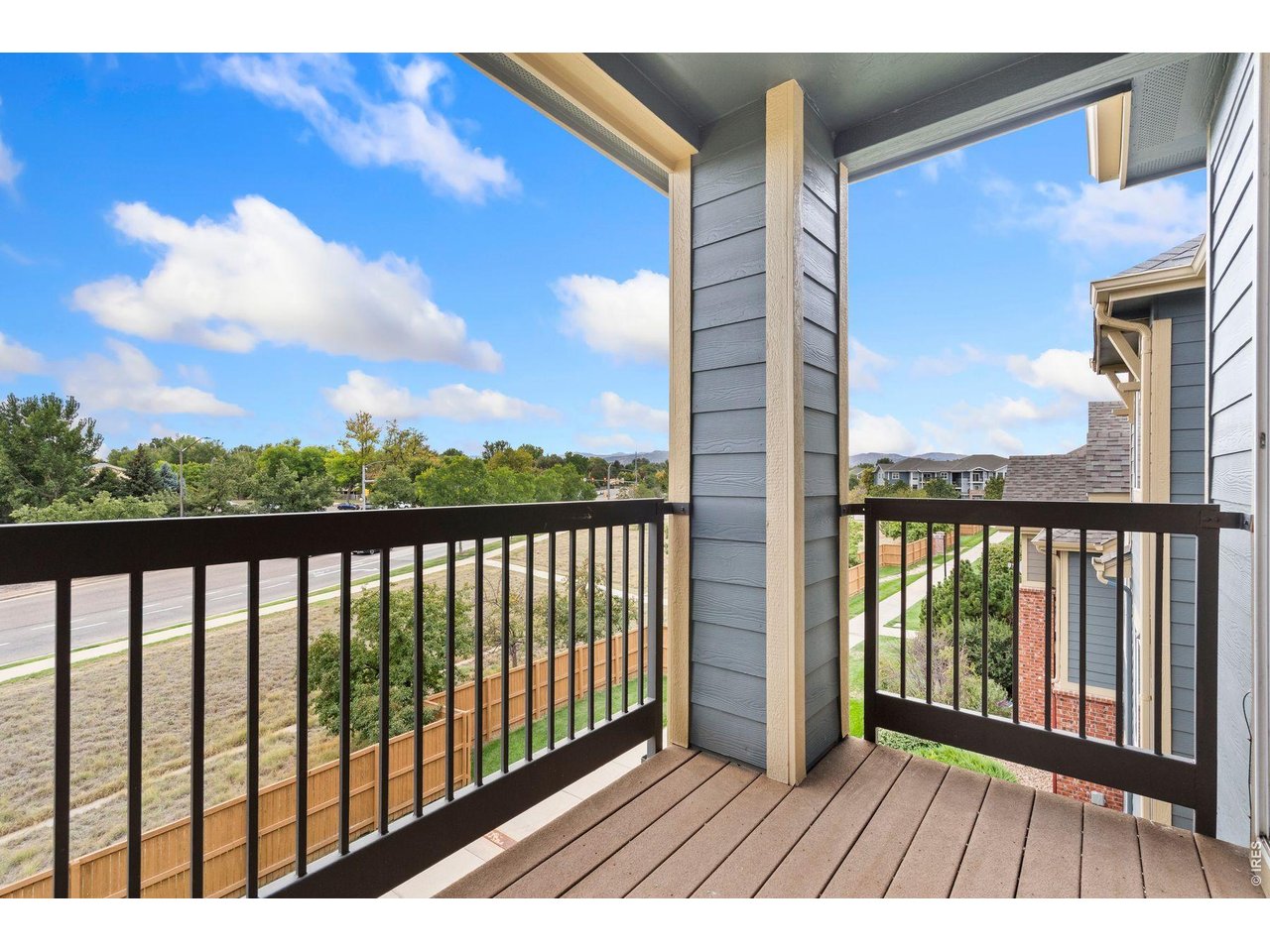 Apartment balcony overlooking a road, trees, neighboring buildings, and distant foothills.