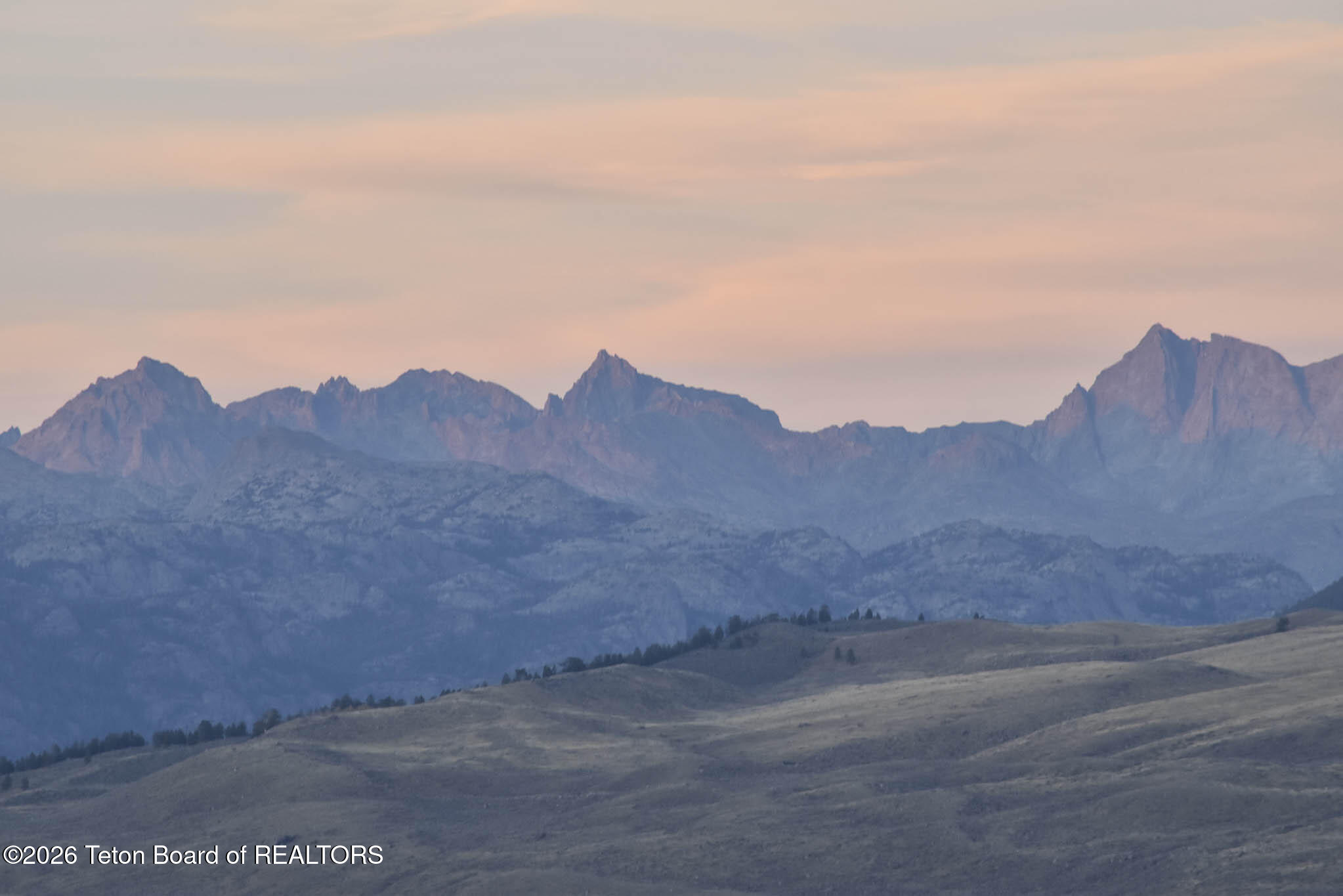 Mountain range beyond rolling grassy hills beneath a pink dusk sky.