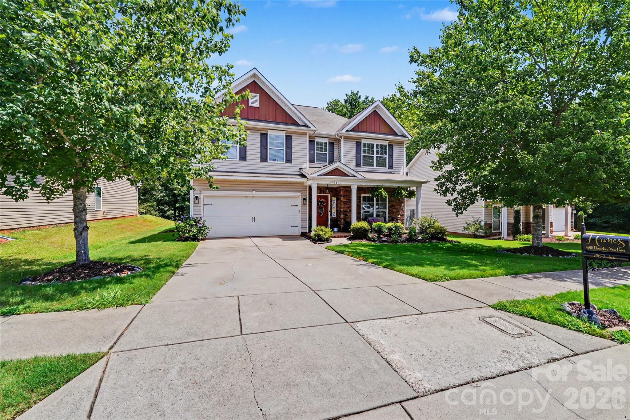 Two-story home with red gables, brick entry, two-car garage, and a tree-lined front yard.