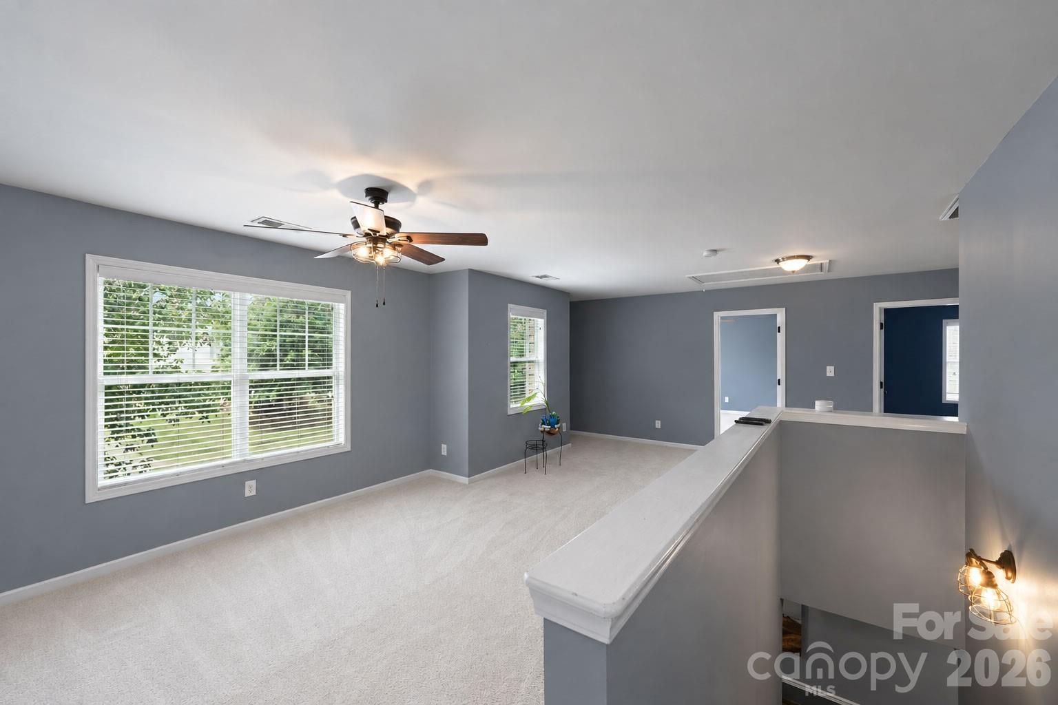 Primary bedroom with gray walls, light carpet, ceiling fan, and a half wall overlooking the stairs.