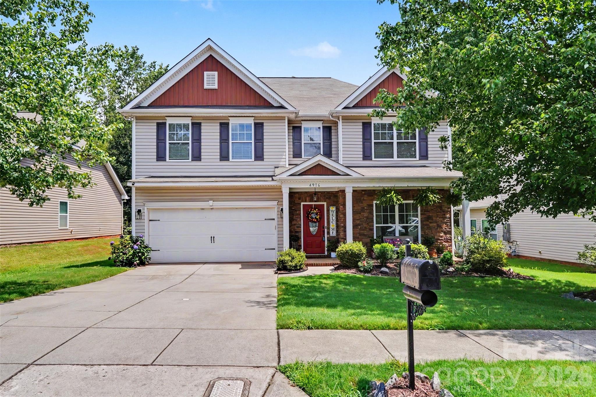 Two-story house with red gables, a stone-front porch, an attached garage, and a landscaped lawn.